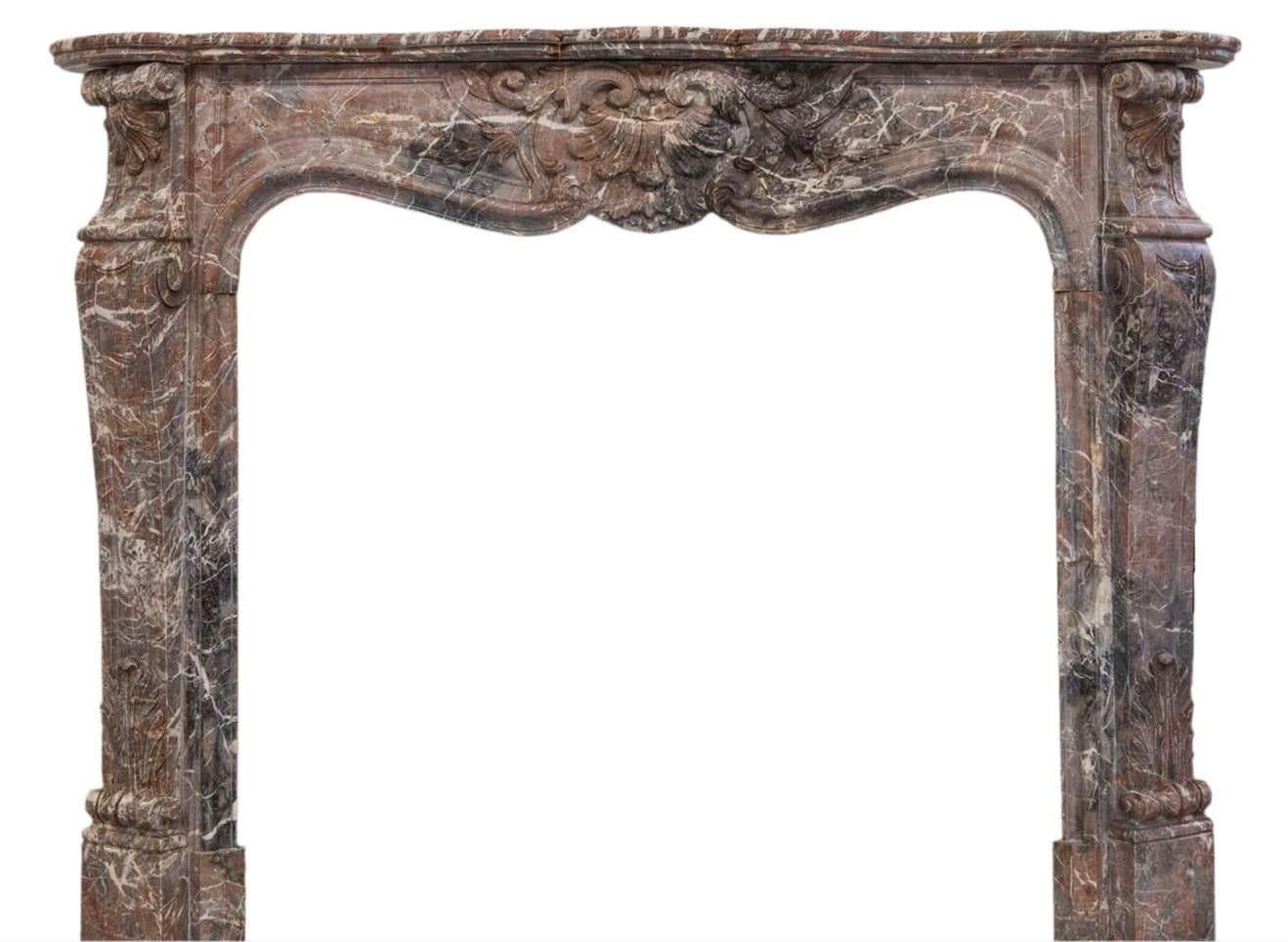 19th century Louis XV style beautiful fireplace sculpted in a soft colored Rouge Royal marble. The finely carved shelf rests on a serpentine front, with a rocaille shell framed by flowers. The jambs are hand carved in the form of curved and tapered