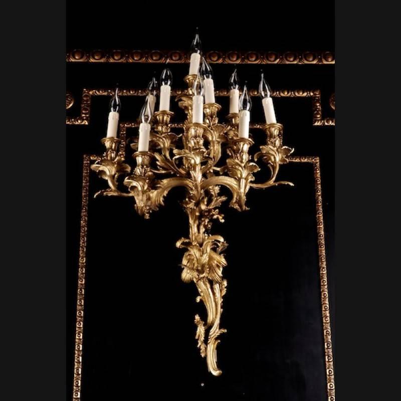 An important, monumental Rococo wall applications in the style of the 18th century. Ten-lighted luminaire. Bronze chiselled. Flat wall sign made from reliefed volutes and acanthus leaves. In the middle of it, ten curved luminaries with an analogous