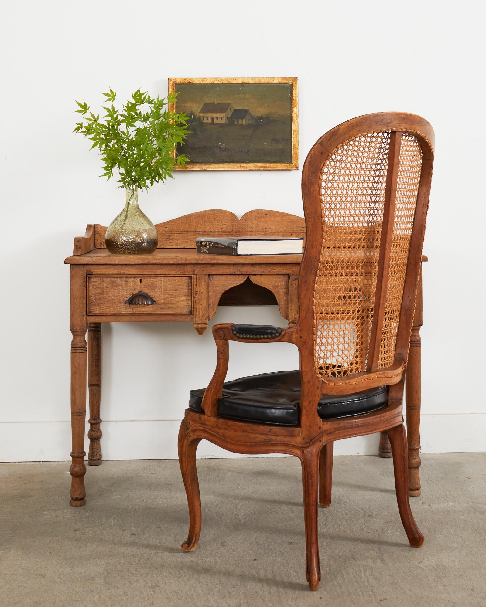 Distinctive 19th century French fauteuil armchair or hall chair featuring a rare high caned back. Beautifully crafted from walnut with a rich aged patina on the finish. The seat has a fitted seat cushion made from black naugahyde over a caned seat.