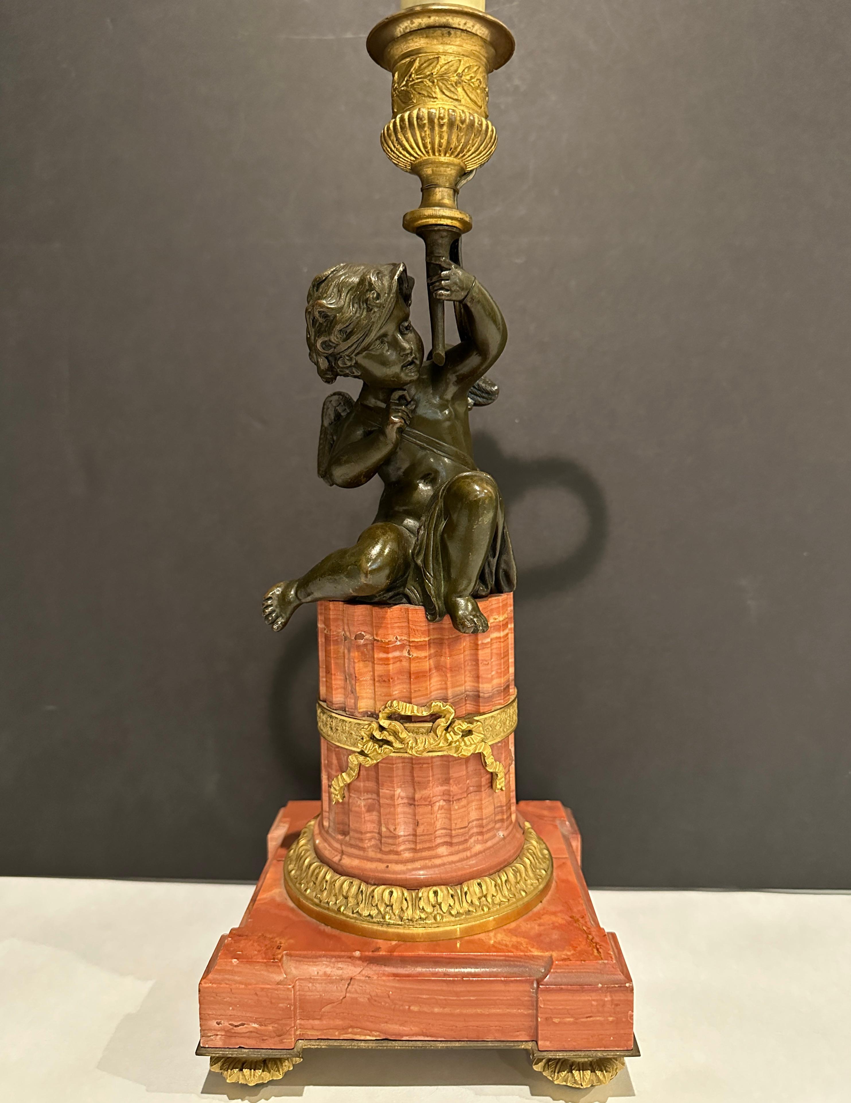 Garniture du XIXe siècle finement ciselée et modelée, montée en lampe. Cupidon ailé magnifiquement patiné tenant une coupe au-dessus de sa tête, comme si une torche était levée.  sur un socle en marbre cannelé monté en bronze doré.  Anneau en forme