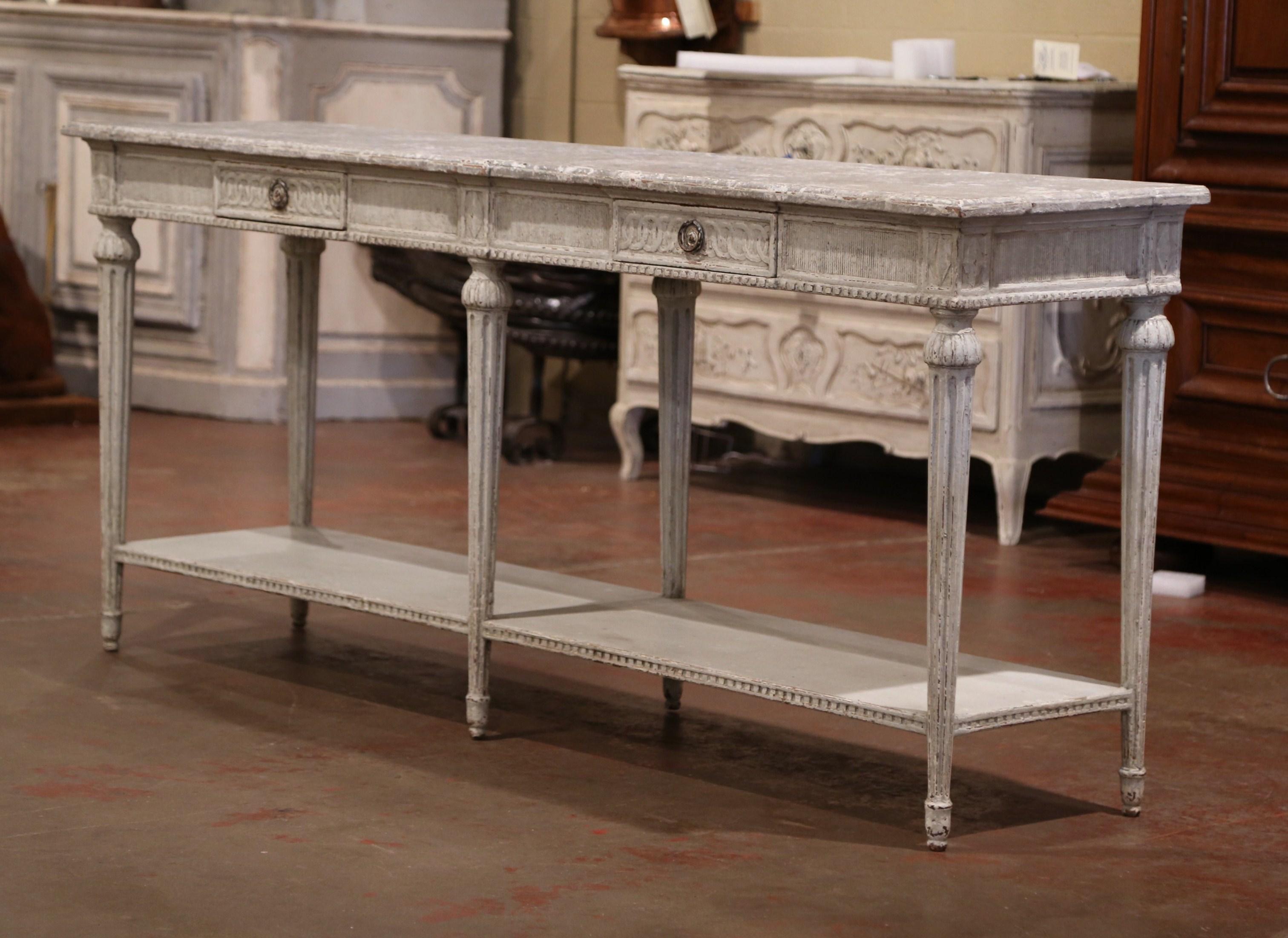 This elegant antique console tables was created in France, circa 1880. The long grey painted table stand on six carved and tapered legs over a carved apron embellished with floral medallions on each corner. The console has two drawers across the