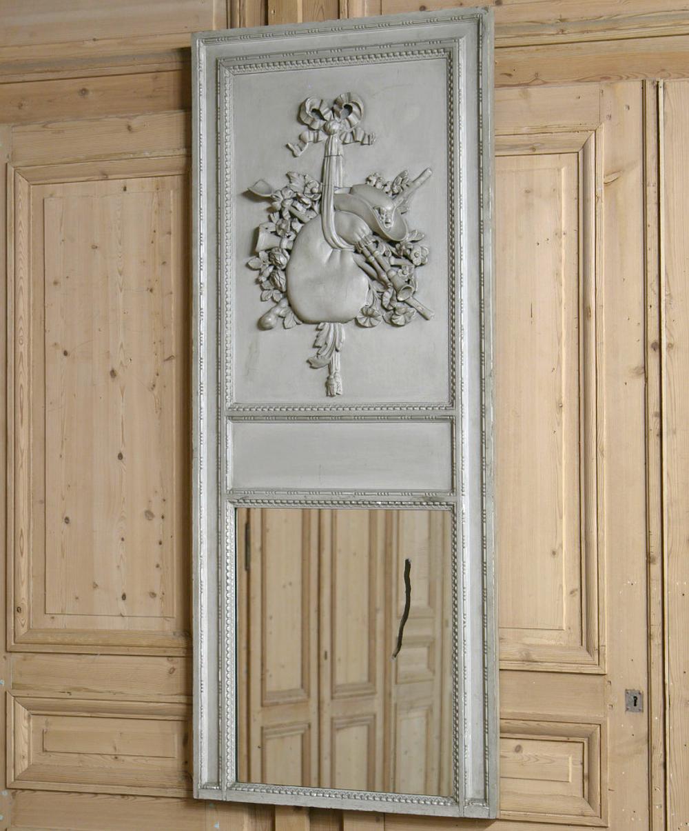 Here is a gorgeous 19th century Country French painted Louis XVI style Trumeau mirror boasting its original patina grey painted finish which has acquired a wonderful patina over the past century. The bold relief on the top panel has been hand carved