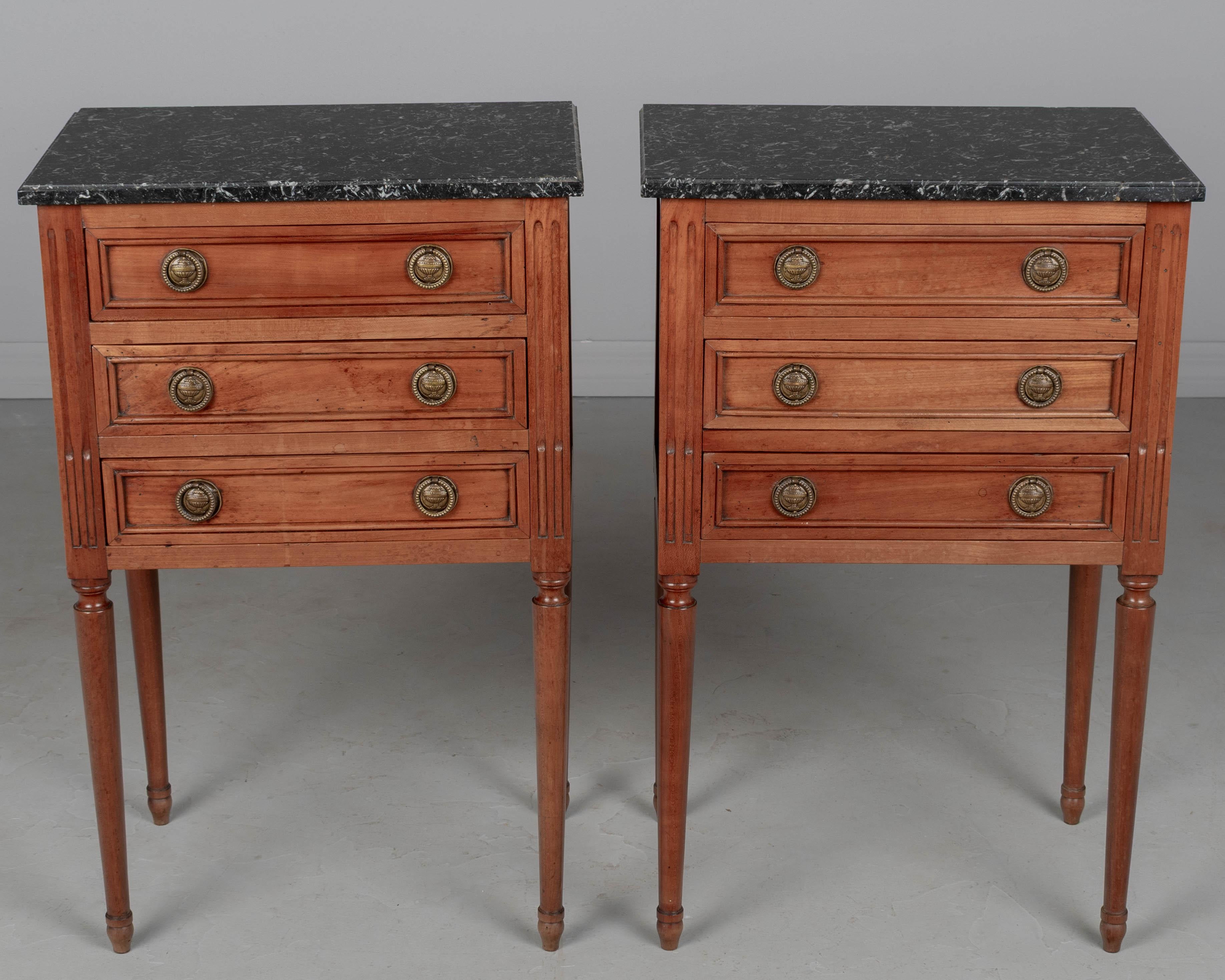 Paire de tables d'appoint ou de chevets en cerisier massif de style Louis XVI français du XIXe siècle. Trois tiroirs à queue d'aronde avec poignées en bronze moulé. Pieds fuselés tournés. Les plateaux en marbre noir ne sont pas attachés, l'un d'eux