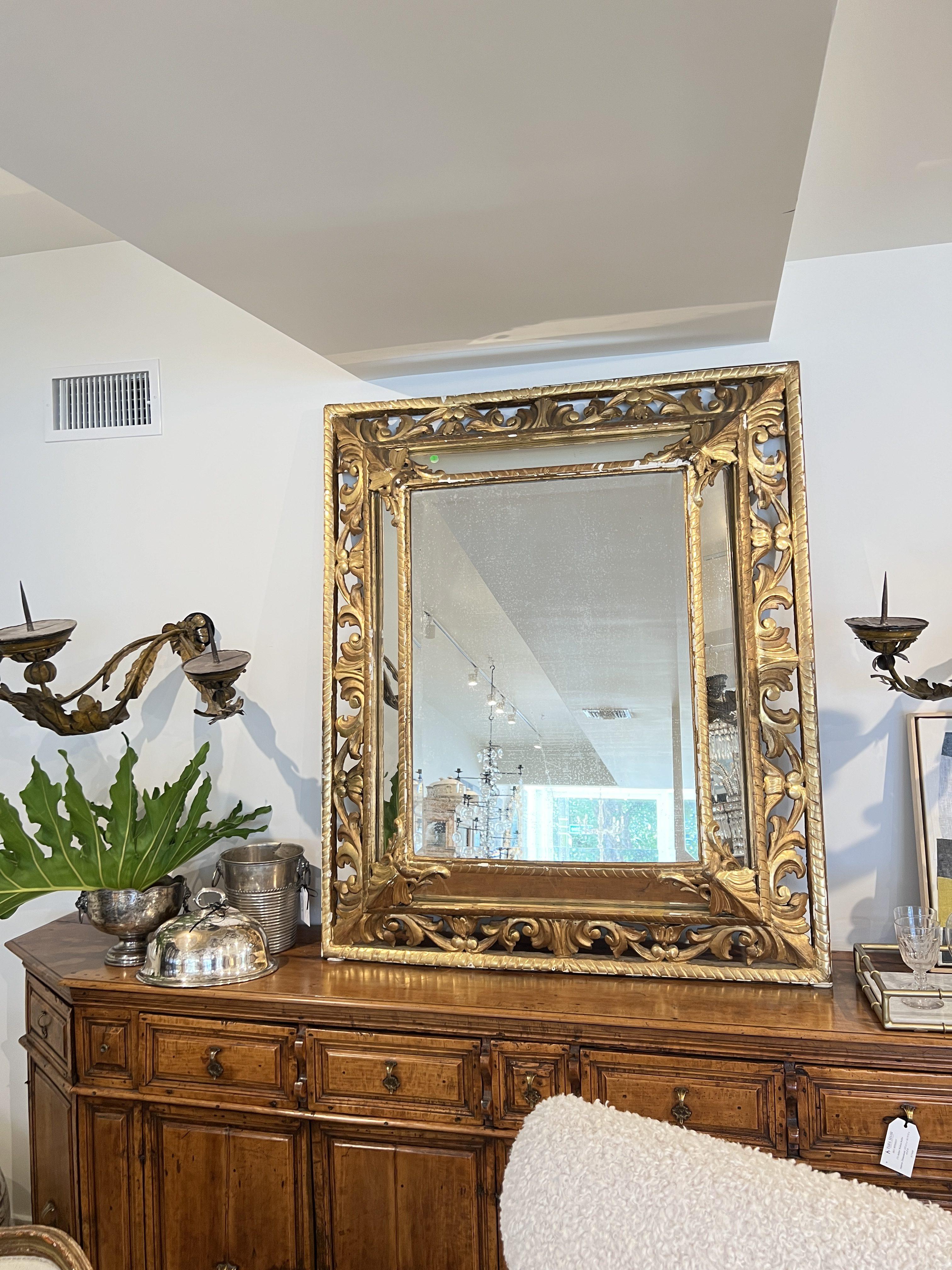 Un élégant miroir antique doré de style Louis XVI, avec un cadre richement sculpté de motifs néoclassiques et une large bordure de verre biseauté, offrant une symétrie intemporelle, une ornementation raffinée et une sophistication lumineuse.