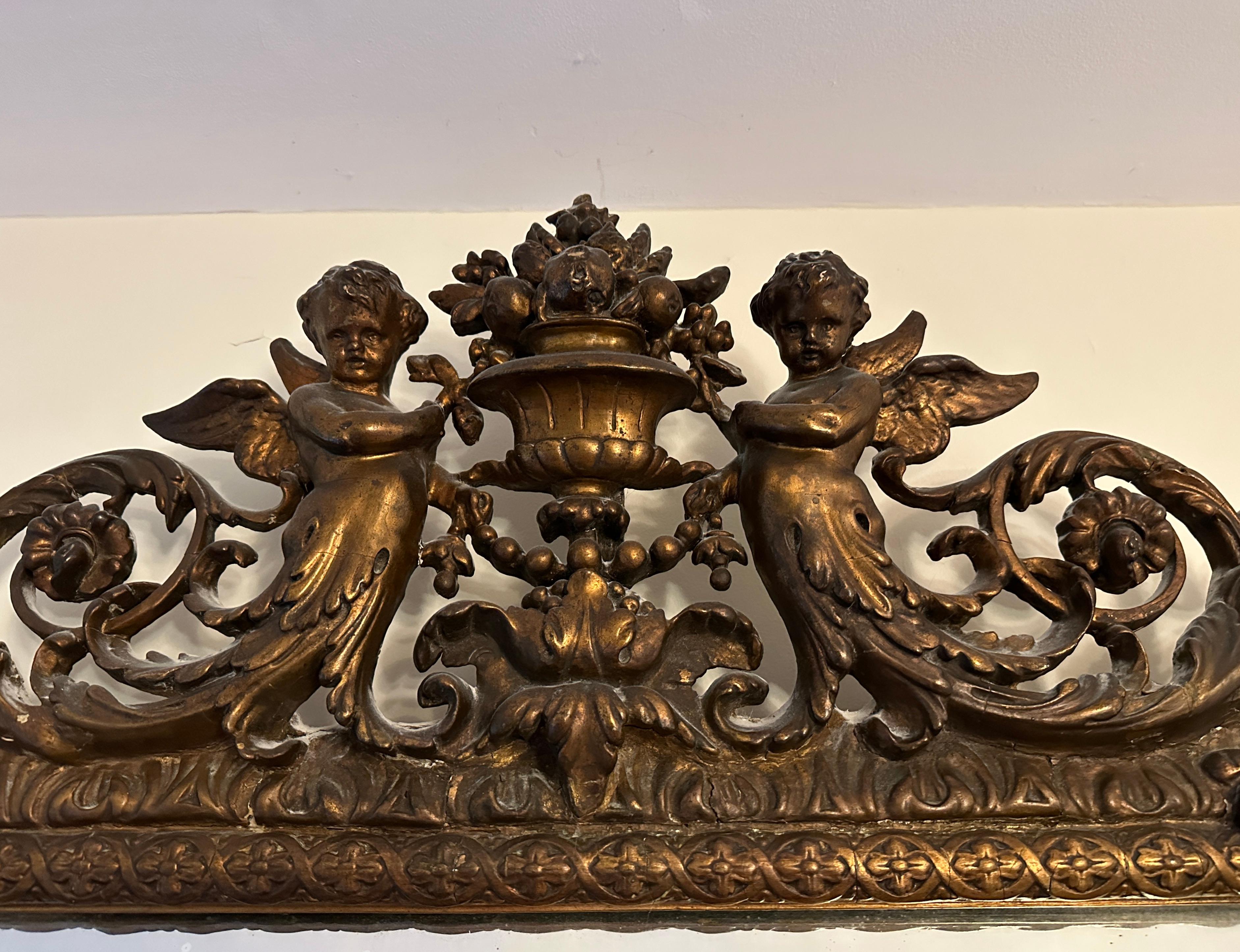 Grand et beau miroir mural doré de style Louis XVI. Le haut du cadre est orné d'une urne centrale et de fleurs flanquées de deux cupidons ailés. Cadre de miroir de forme coussin à sept panneaux, séparés par des éléments Louis XVI. Belle patine