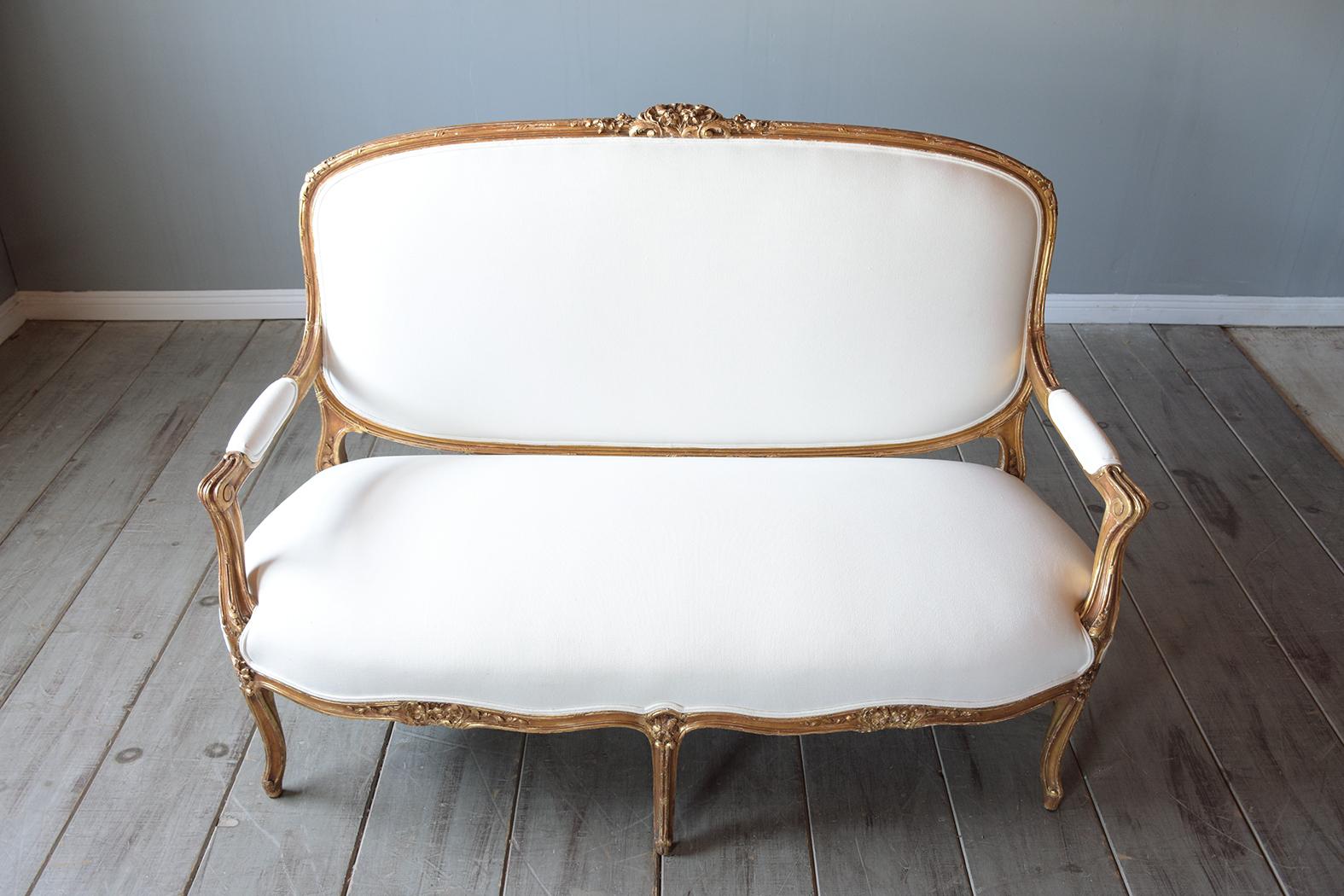 This 19th-century Louis XVI sofa is handcrafted out of maple wood and has been completely restored by our team of expert craftsmen. This antique sofa features a hand-carved frame with carved flower & leaves details along the top/bottom, comes with