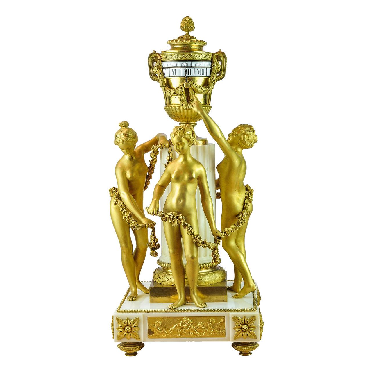 Pendule de cheminée de style Louis XVI en bronze doré et marbre blanc
D'après un modèle d'Étienne-Maurice Falconet
La pendule à cercles tournants, en forme d'urne, est soutenue par une colonne de marbre cannelée où sont représentées les Grâces