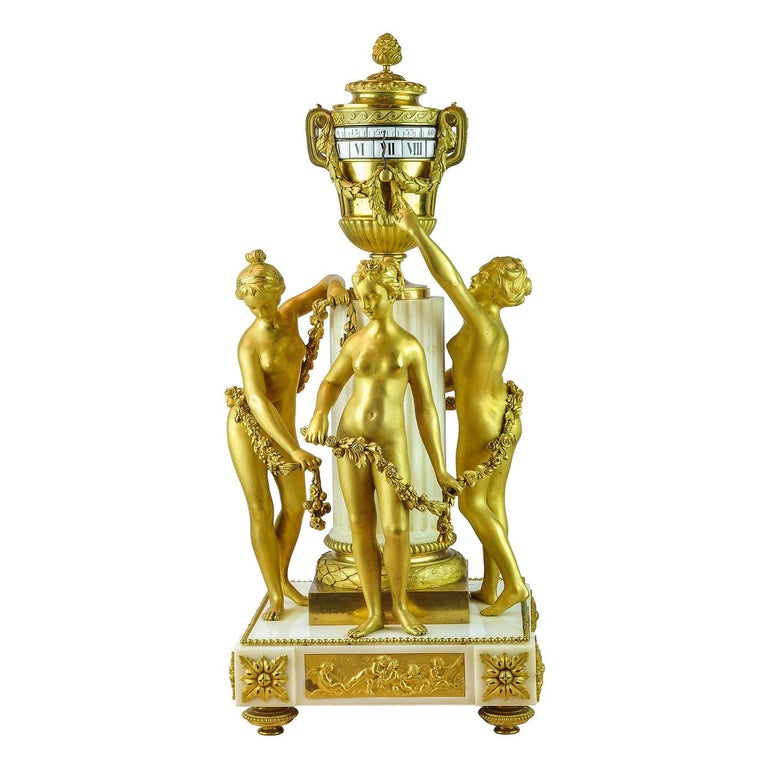 A Fine Louis XVI-Style Gilt Bronze and White Marble Mantel Clock
After a model by Étienne-Maurice Falconet
The urn-form pendule à cercles tournants supported by a fluted marble column attended by the Graces indicating the time, the circular
