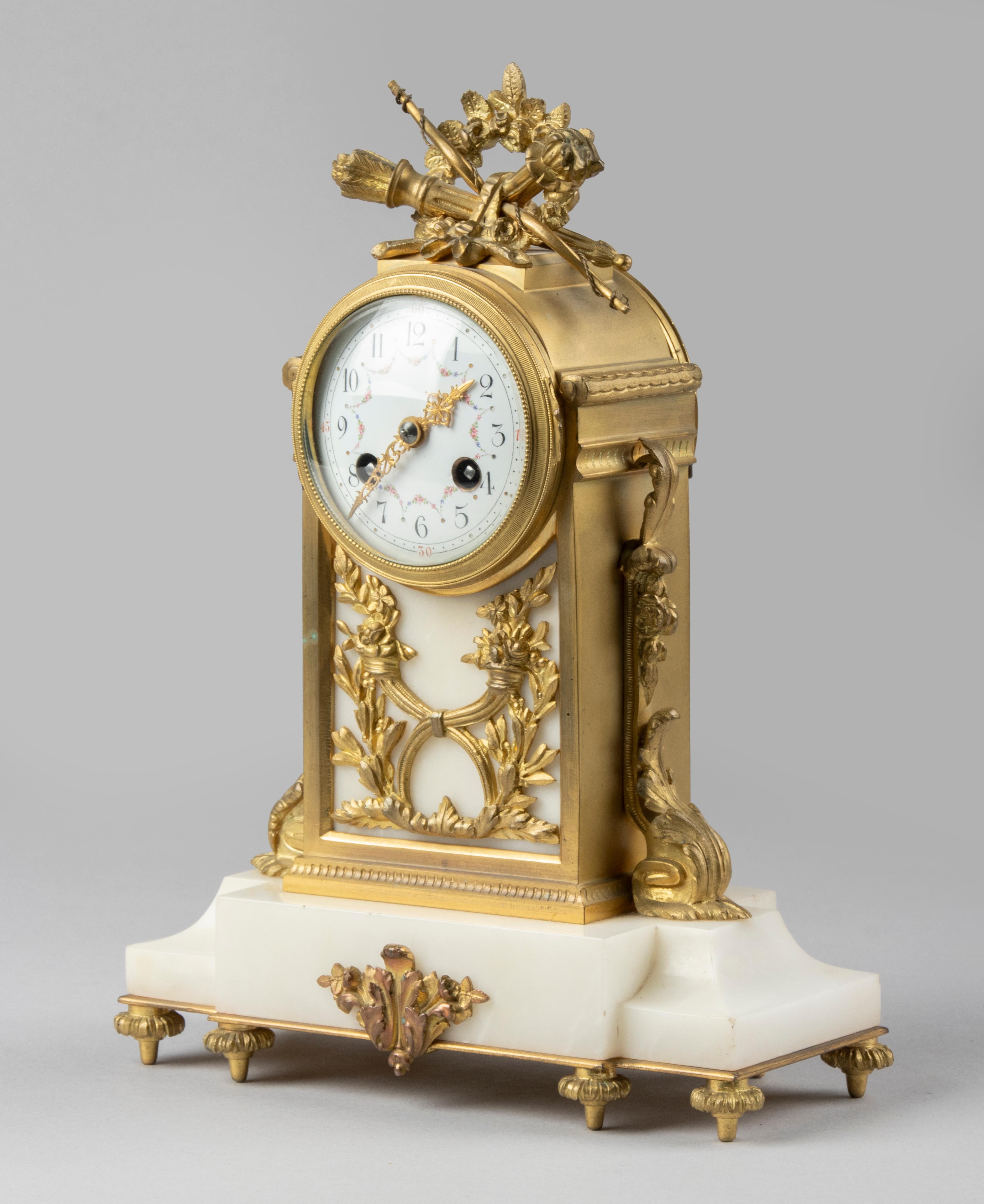 A French Louis XVI style bronze ormolu mantel clock. The case is made of gilt brass and bronze ormolu casted ornaments. Enameled dial with hours and minutes in Arabic numerals. Embellished with neo-classical ornaments, the upper part decorated with