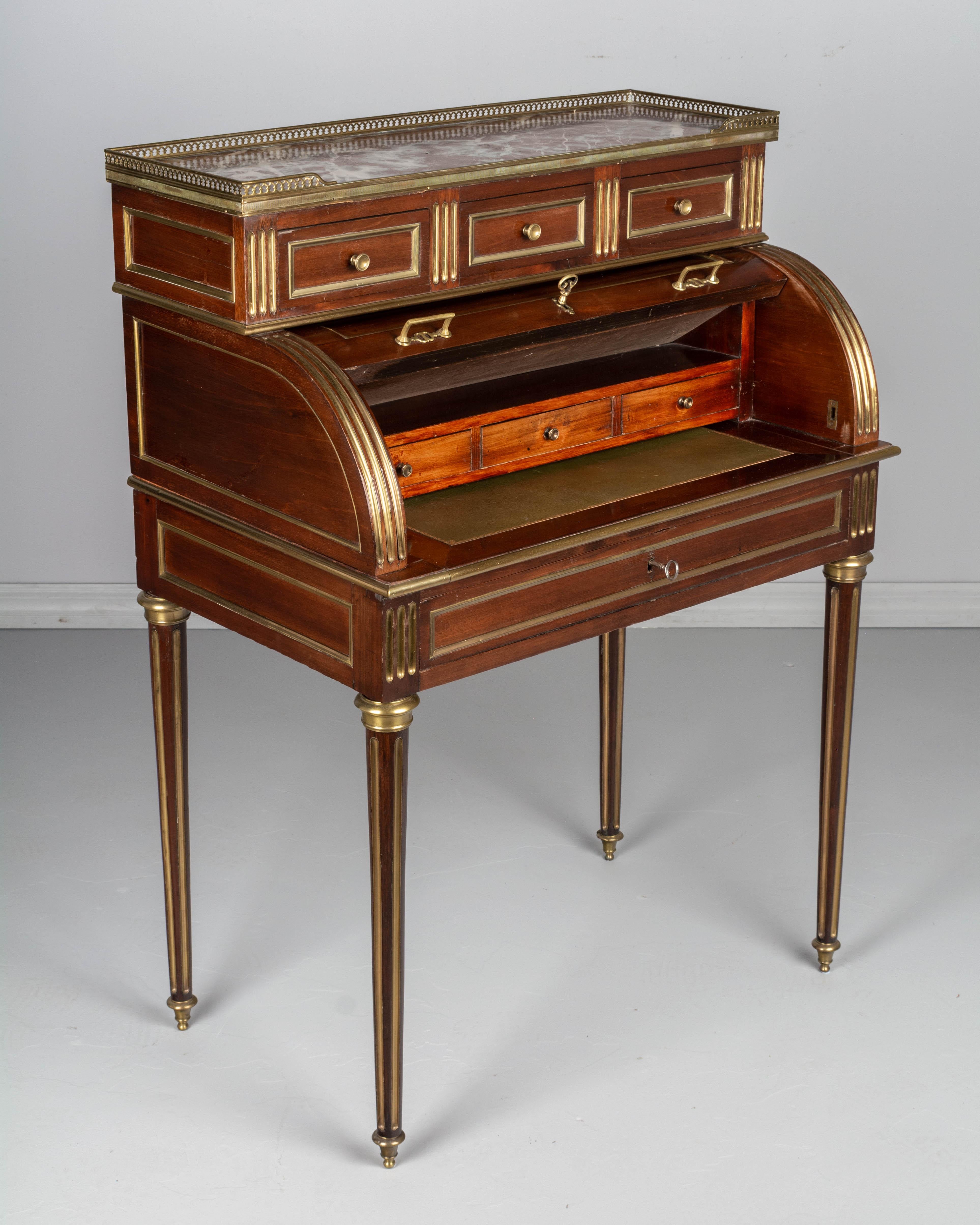A 19th century Louis XVI style French bureau à cylindre, or roll top desk, made of solid and veneer of mahogany with brass trim and hardware. Good proportions and nice profile to this small desk. Roll top opens to a pull-out writing table with green