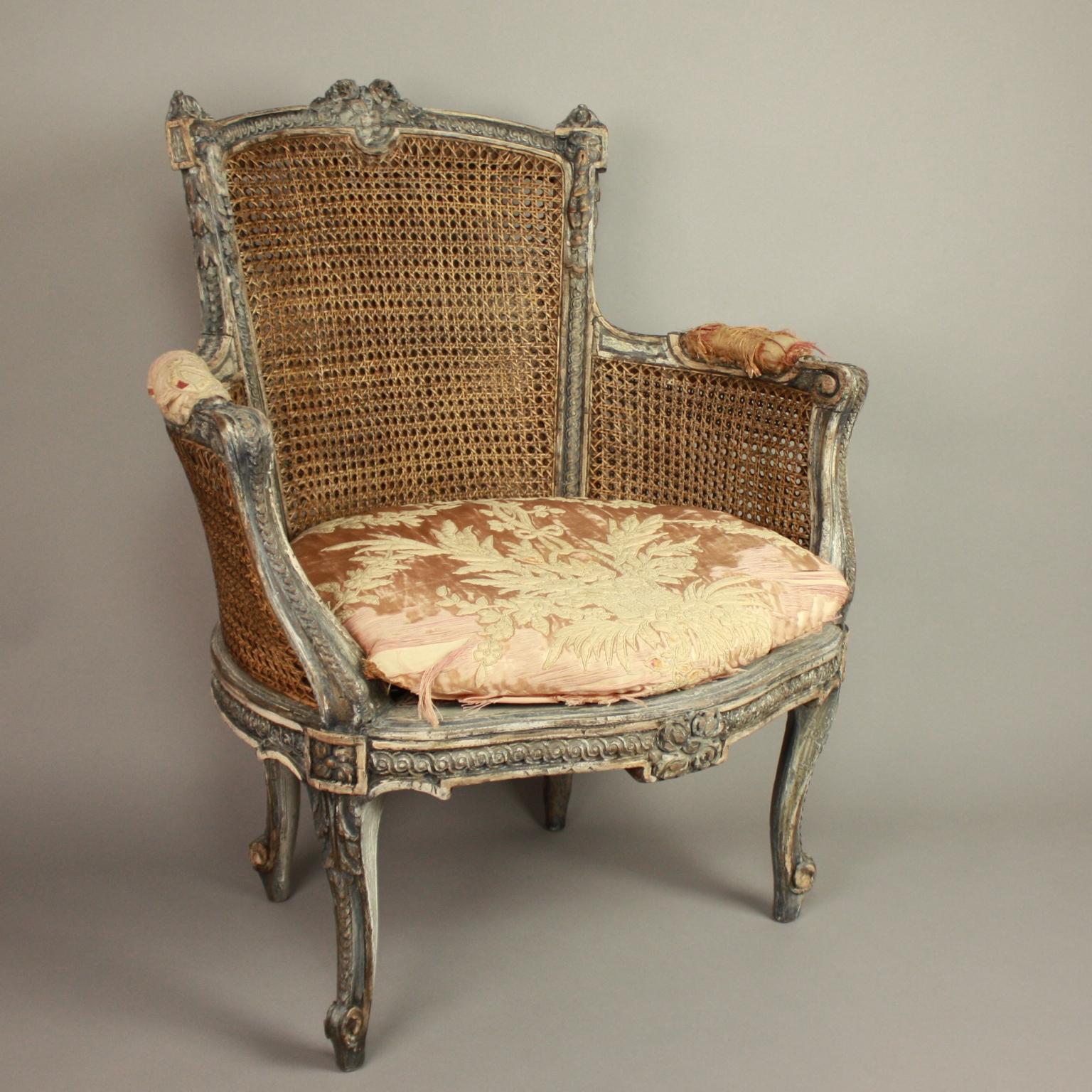 A 19th century Louis XVI style caned and painted bergere, with double caned back and sides, the frame carved with ribbon and guilloche ornament, painted in grey and white, resting on cabriole legs. The loose seat cushion upholstered with an