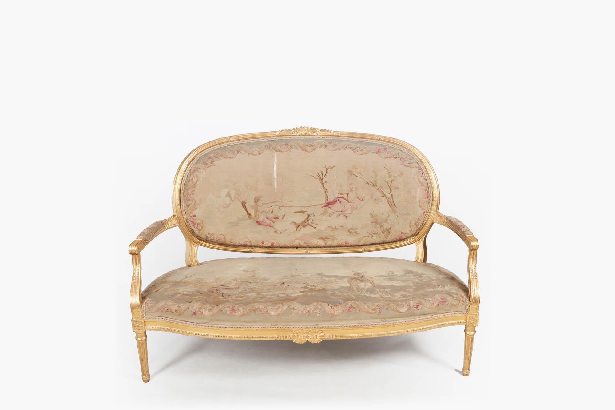 19th century Louis XVI style carved five piece gilt salon suite consisting of canapé sofa and four fauteuil chairs all complete with tapestry upholstery.

The sofa with giltwood frame has an oval ribbon carved back, and shaped padded armrests
