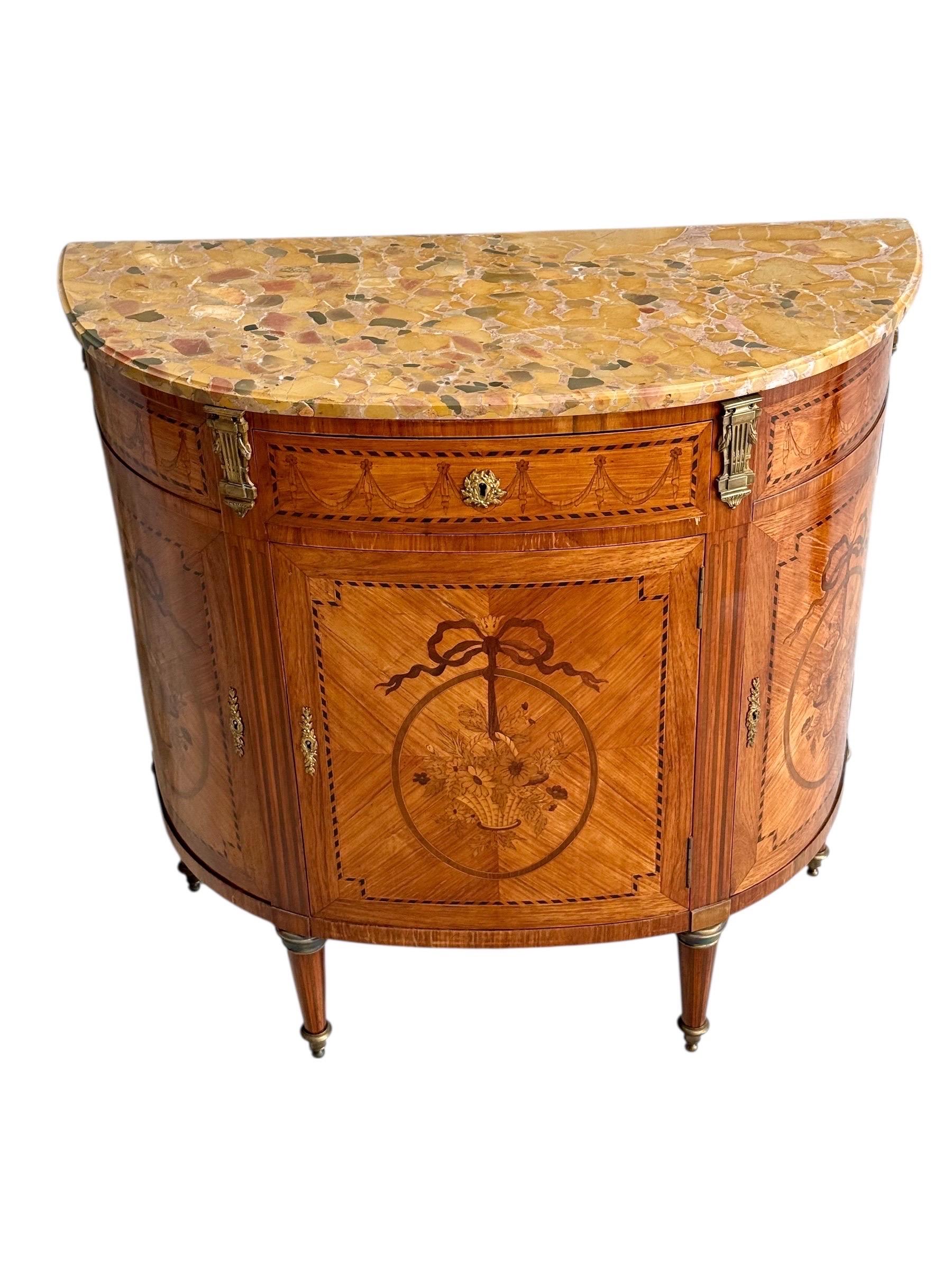 Elegante cómoda demiluna estilo Luis XVI del siglo XIX, finamente trabajada en marquetería y adornada con una encimera de mármol breccia de ricos colores. Esta refinada pieza refleja maravillosamente la inspiración neoclásica de finales del siglo