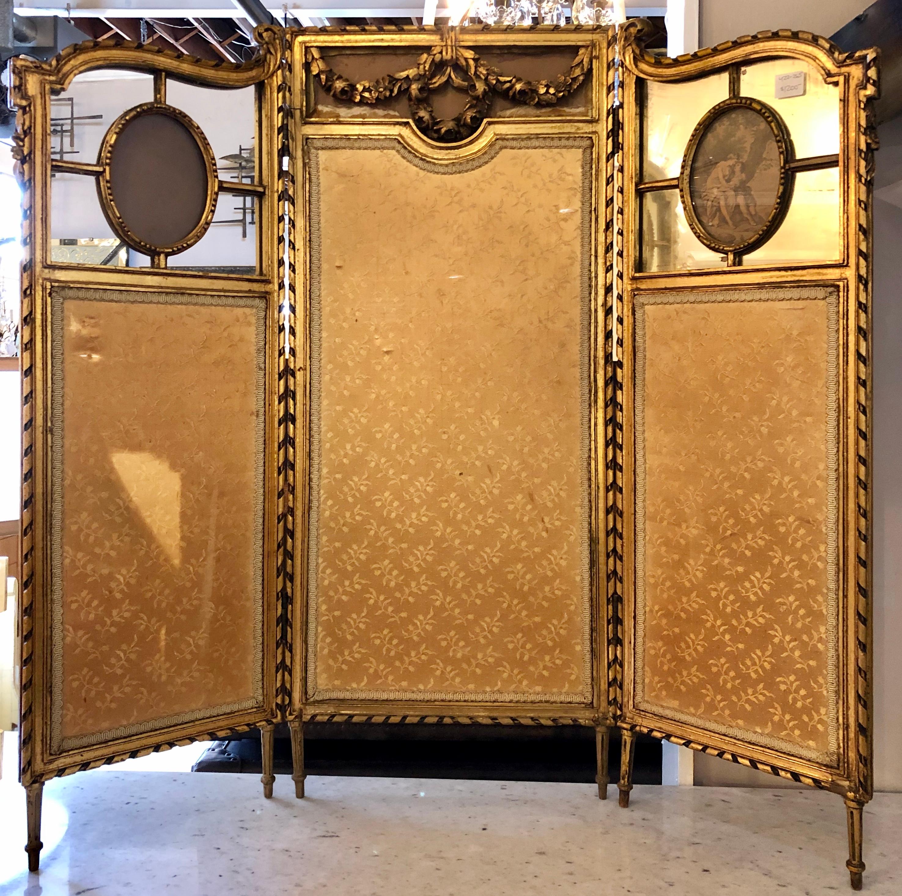 19th century Louis XVI style fire / dressing screen or room divider. This finely carved giltwood room divider or dressing screen has three panels. The center, larger, panel having a fine fabric framed in a carved wood design terminating with laurel