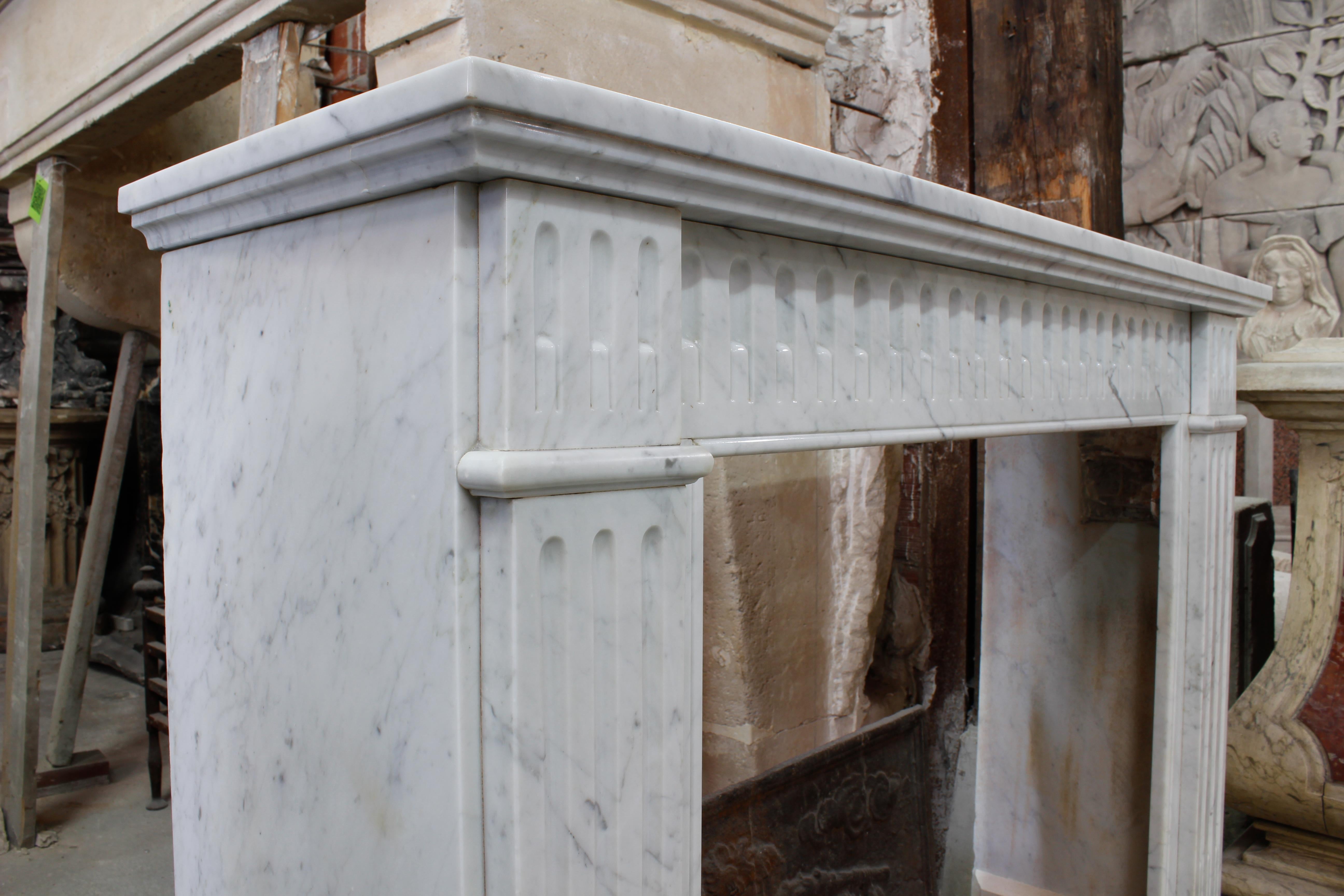 Small antique Louis XVI style fireplace made out of white Carrara marble during the 19th century.
Both jambs and heads are fluted and the entablature is carved with fluting all along its length.

