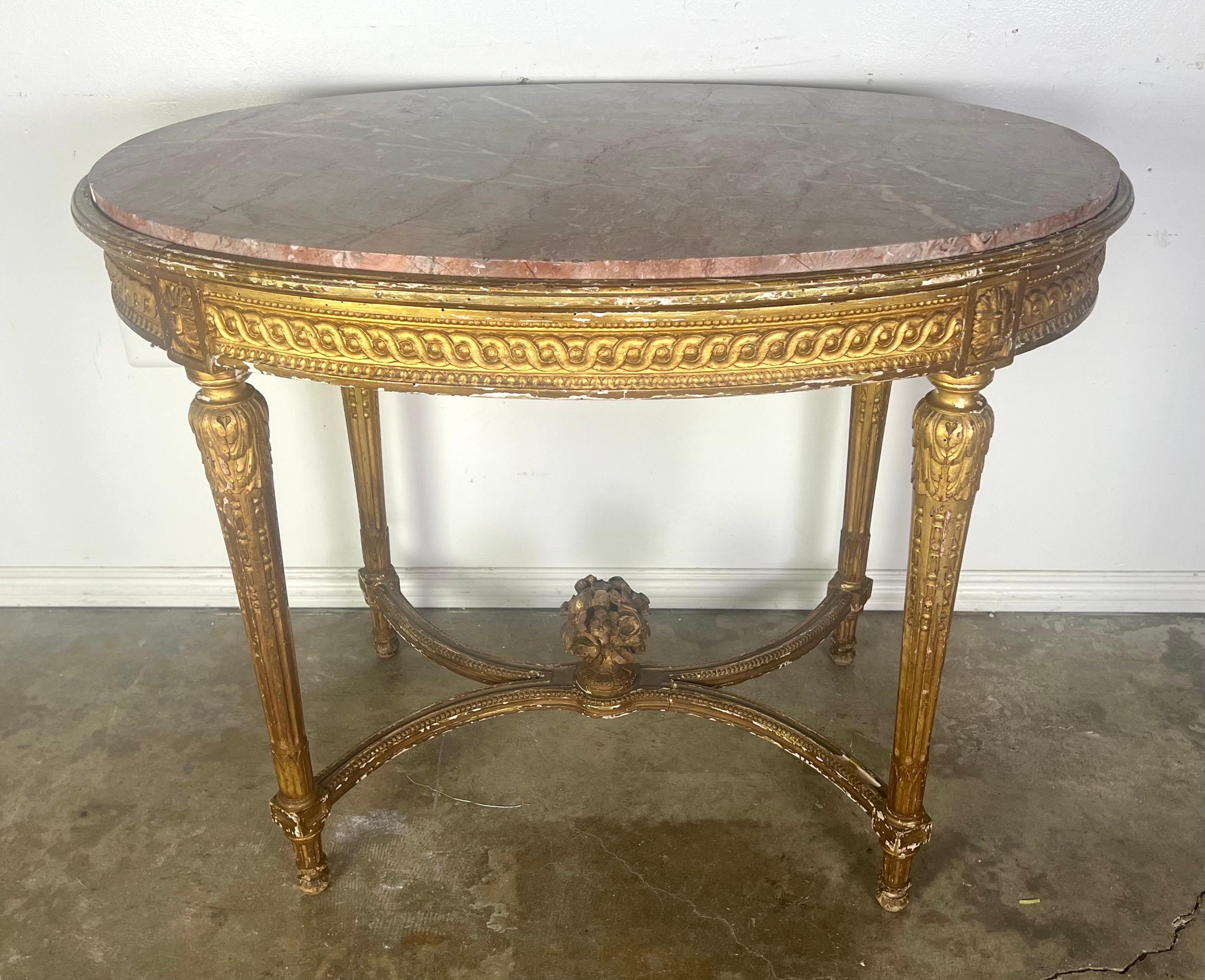 19th Century Louis XVI style oval table with marble top.  The table's gilt wood frame showcases the sophisticated restraint typical of Louis XVI style furniture, with a focus on straight lines and balanced proportions.  The four straight legs,
