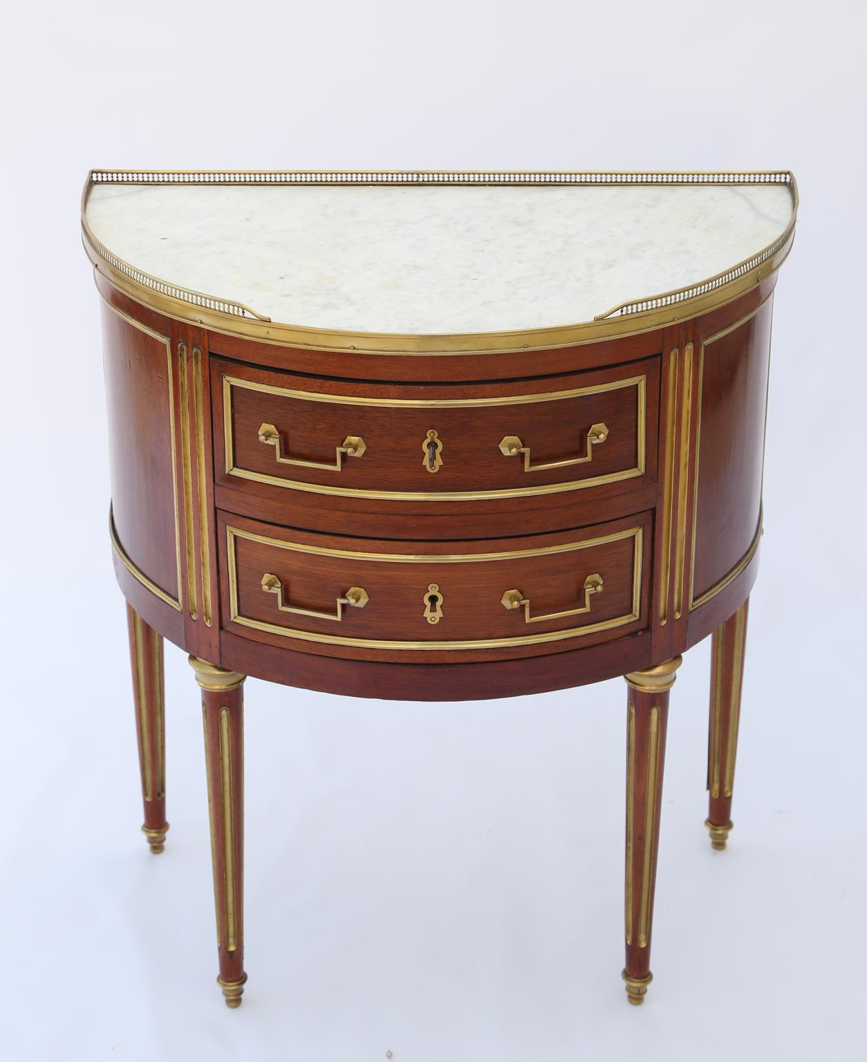 Demilune chest, having its original top of Carrara marble, surrounded by 3/4 pierced gallery, over double stacked drawers, its fielded front and sides framed in brass, raised on round, tapering, brass-inset fluted legs, ending in touipe feet.