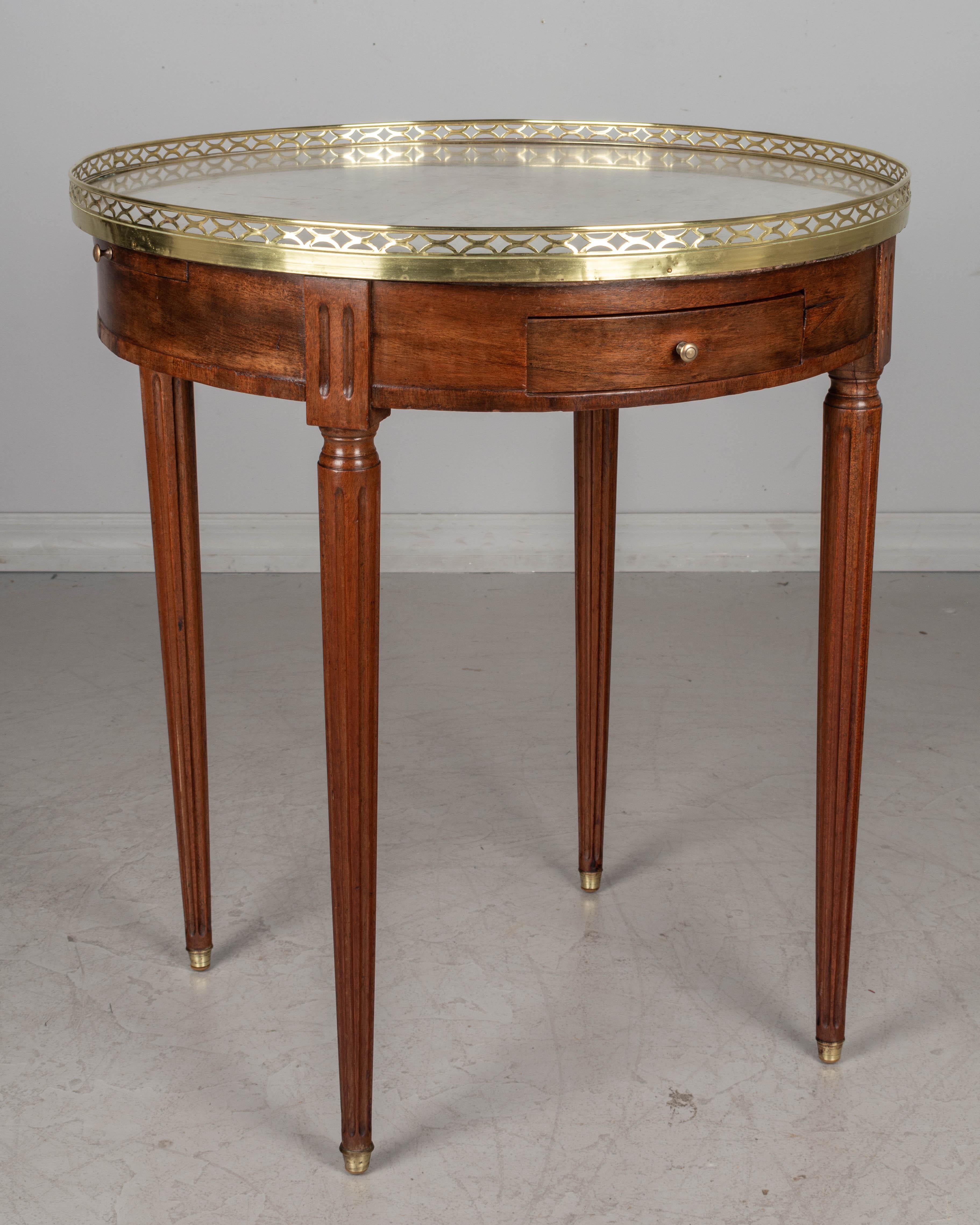 A 19th century Louis XVI style bouillotte table made of mahogany with fluted legs ending in brass sabots. Original white veined marble top with polished brass gallery. Two dovetailed drawers and two pull out shelves with green leather surface. All