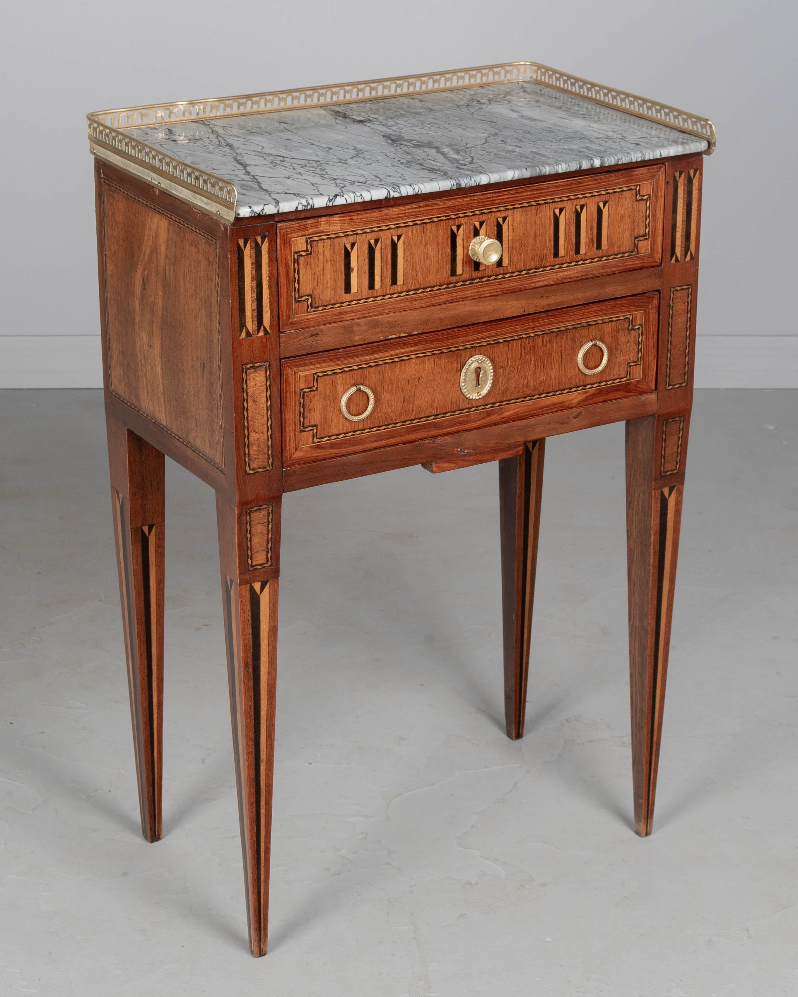 A 19th century French Louis XVI style marble top marquetry side table, or nightstand, made of veneers of mahogany and walnut. Two drawers with cast brass hardware. Beautiful blue tarquin veined marble top with polished brass gallery. Slender tapered