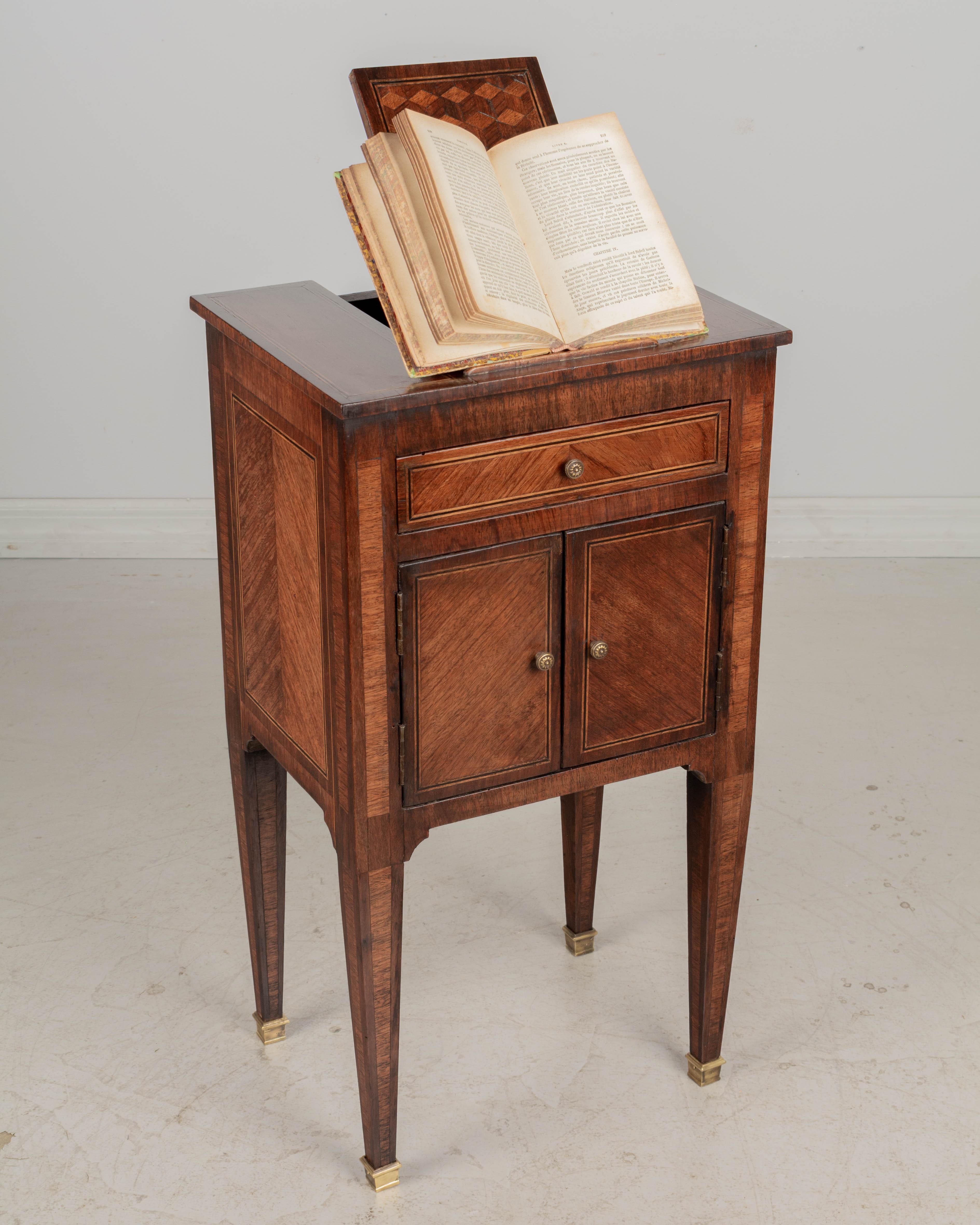 A 19th century French Louis XVI style marquetry side table, or nightstand, with an unusual book stand, or easel that props open on the top. One dovetailed drawer above cabinet doors. Made of inlaid veneer of various woods, mainly mahogany. Slender