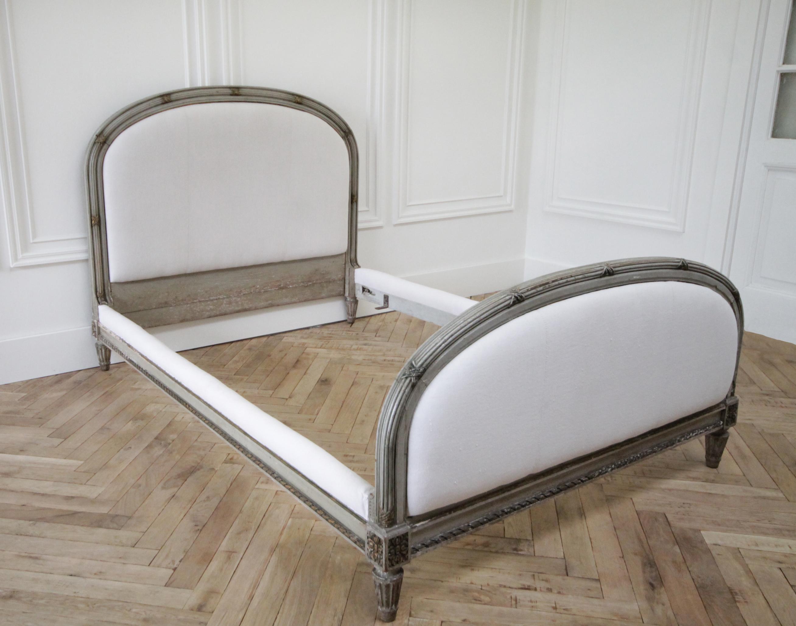 19th century Louis XVI style painted and upholstered full size bed
Original painted patina finish in grayish tones, with subtle distressed edge, and gilt wood painted accents.
Upholstered in antique white French linen metis linen fabric, this