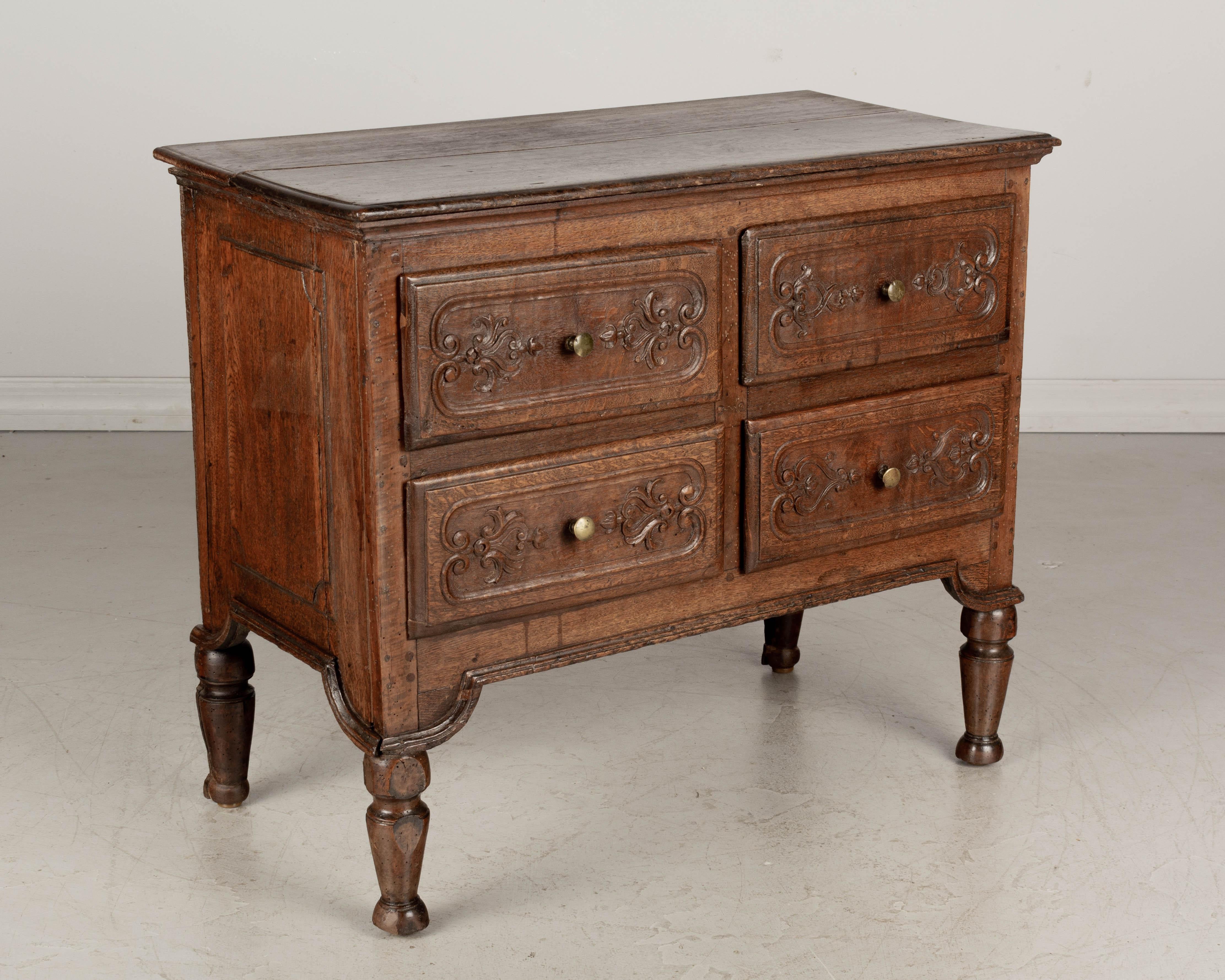 An early 19th century Louis XVI style petite French commode, or chest of drawers made of solid oak. This small commode has carved relief adorned drawers and sturdy turned legs. Waxed patina. Probably from Alsace. A good size for use as a nightstand.