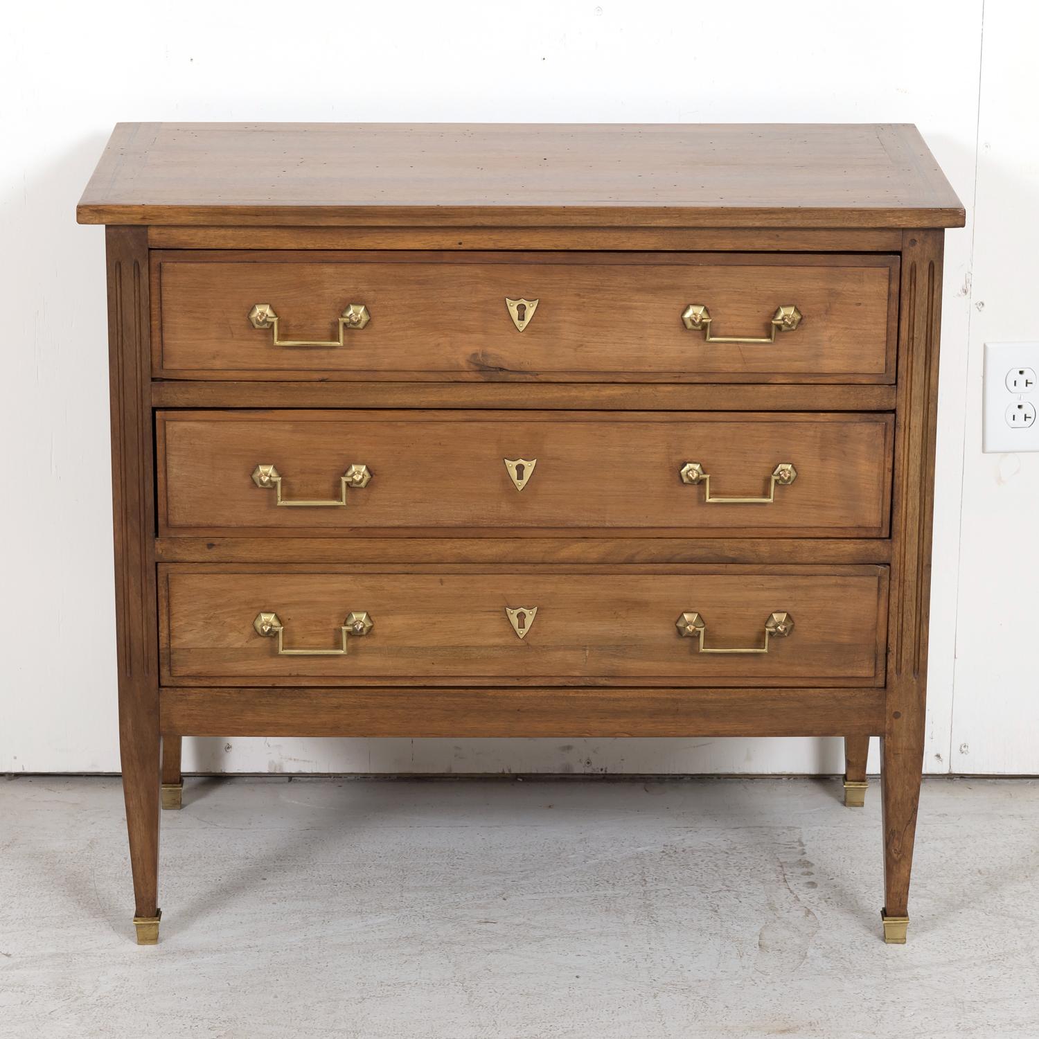A late 19th century French Louis XVI style petite commode handcrafted of walnut by talented artisans in the port city of Bordeaux, circa 1880s, having a rectangular top with a marquetry band sitting above three drawers adorned with original