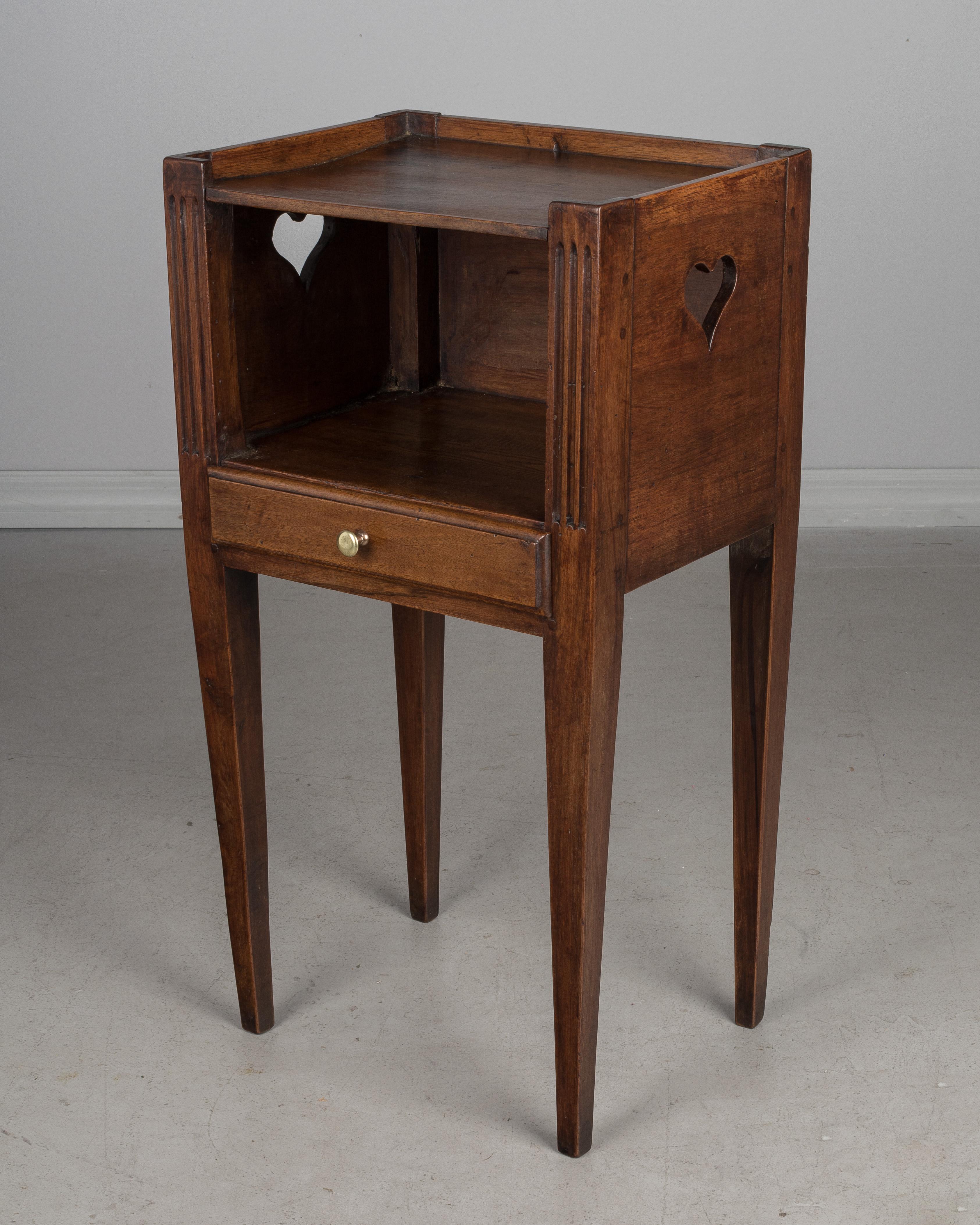 An early 19th century Louis XVI style Country French side table or nightstand made of solid walnut, with pierced heart shaped cut-outs on the sides. Open niche and a shallow drawer with a brass knob. Knob is old but not original. Slender tapered