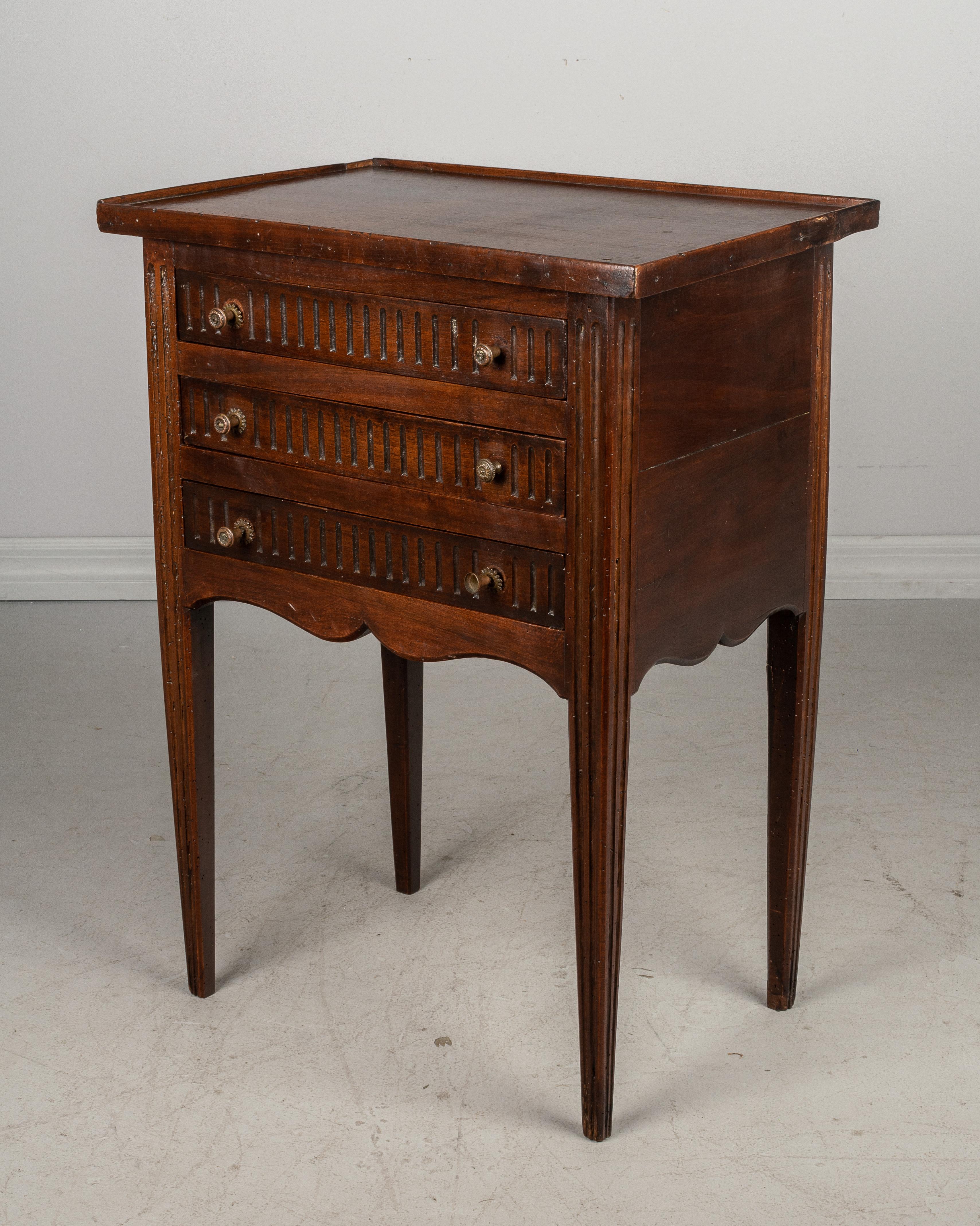 A 19th century French Louis XVI style side table made of walnut. Nice proportions with slender legs. Three dovetailed drawers with subtle carved detail. Original brass pulls are as found. Pegged construction. Minor repairs.
 