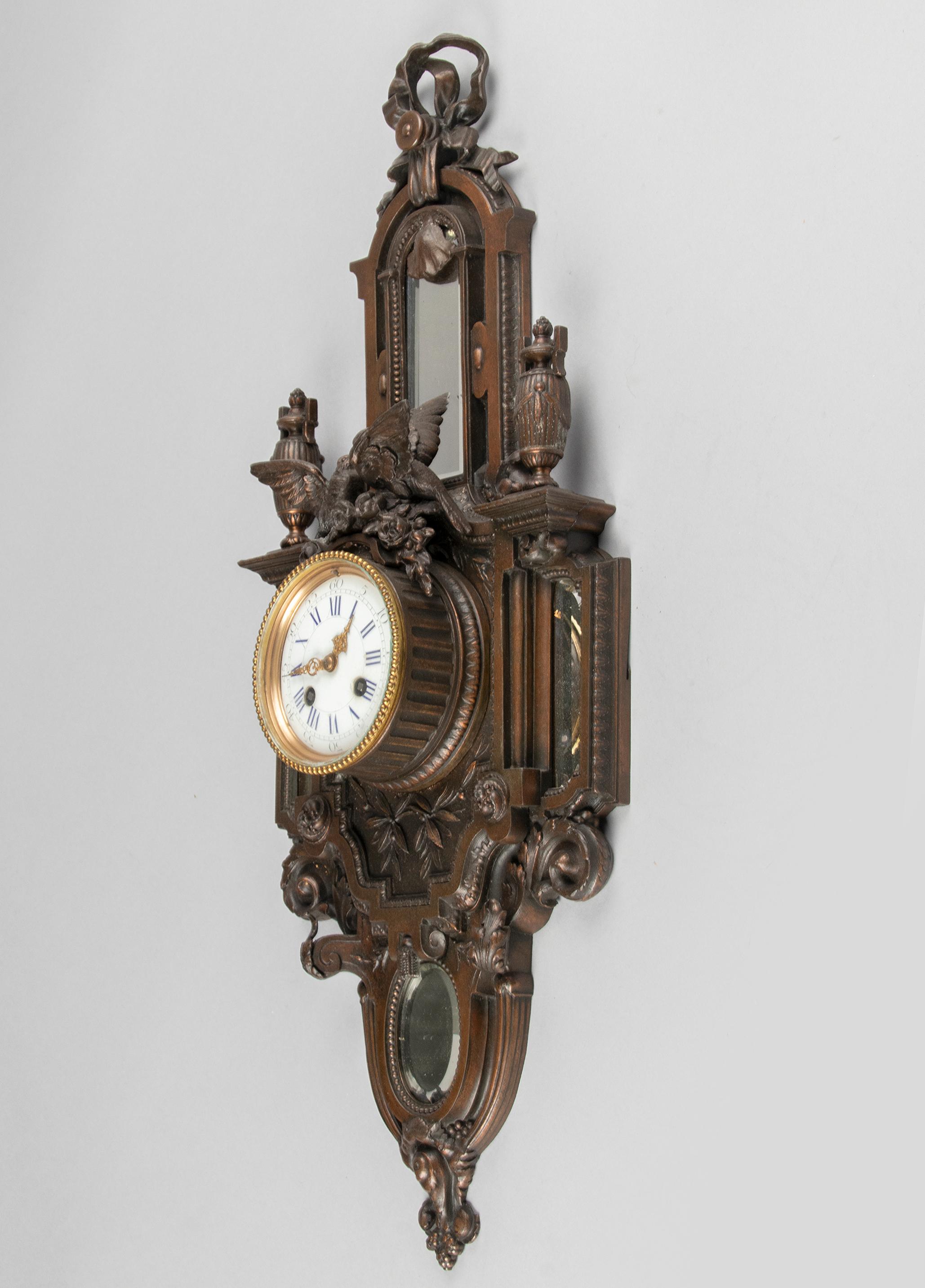 A Louis XVI style cartel wall clock, made in France circa 1880-1890. The case is made of casted spelter (metal alloy) and fitted with four beveled mirror glass. The dial is covered with an enameled finish. Above the clockwork a birdsnest. Richly