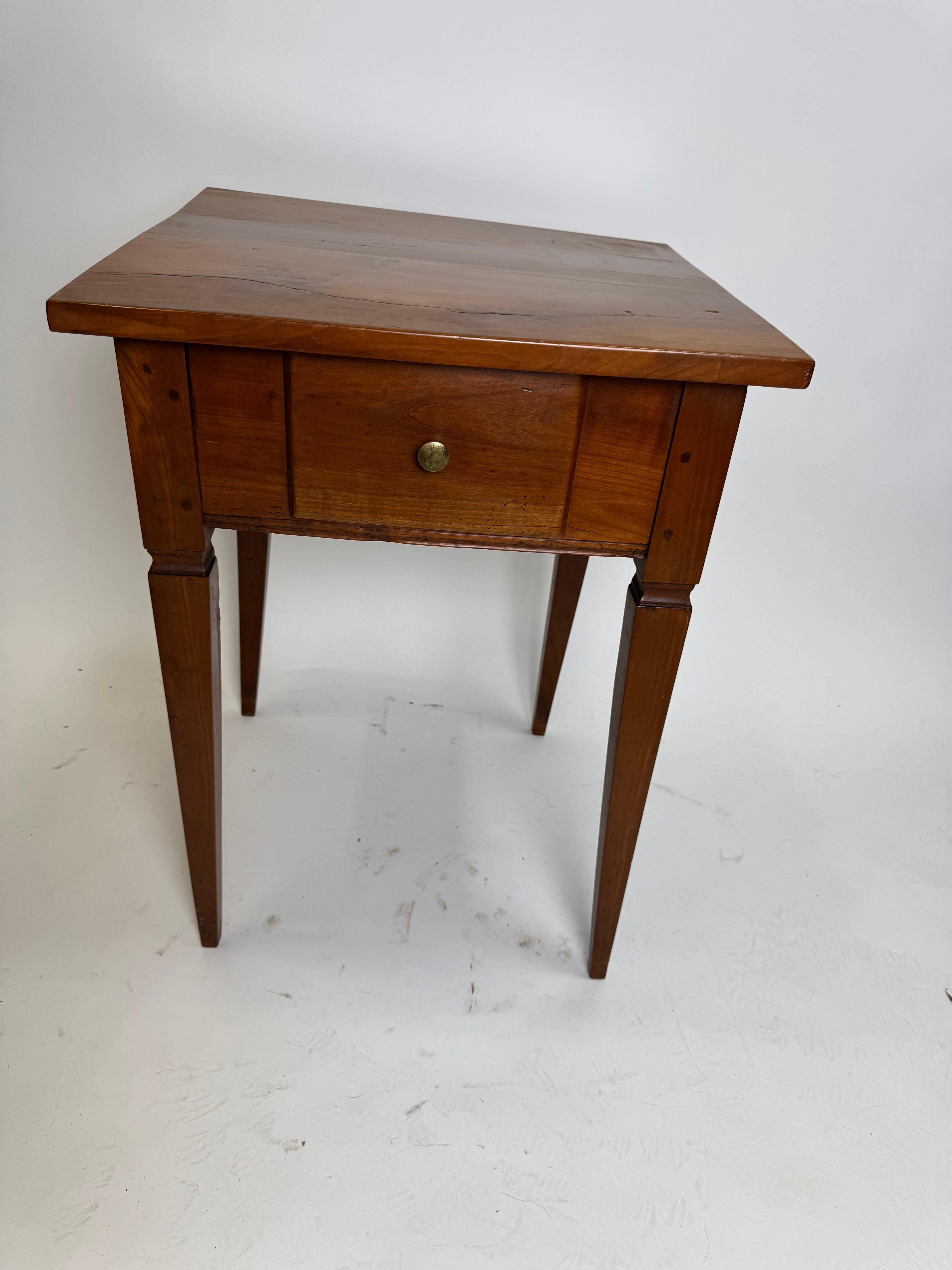 A country Swiss table with a drawer in the French Louis XVI or Neo-Classical style.  
It has a warm walnut finish with pine as a secondary wood with brass pull.  It is very simple but elegant and functional for many uses.  