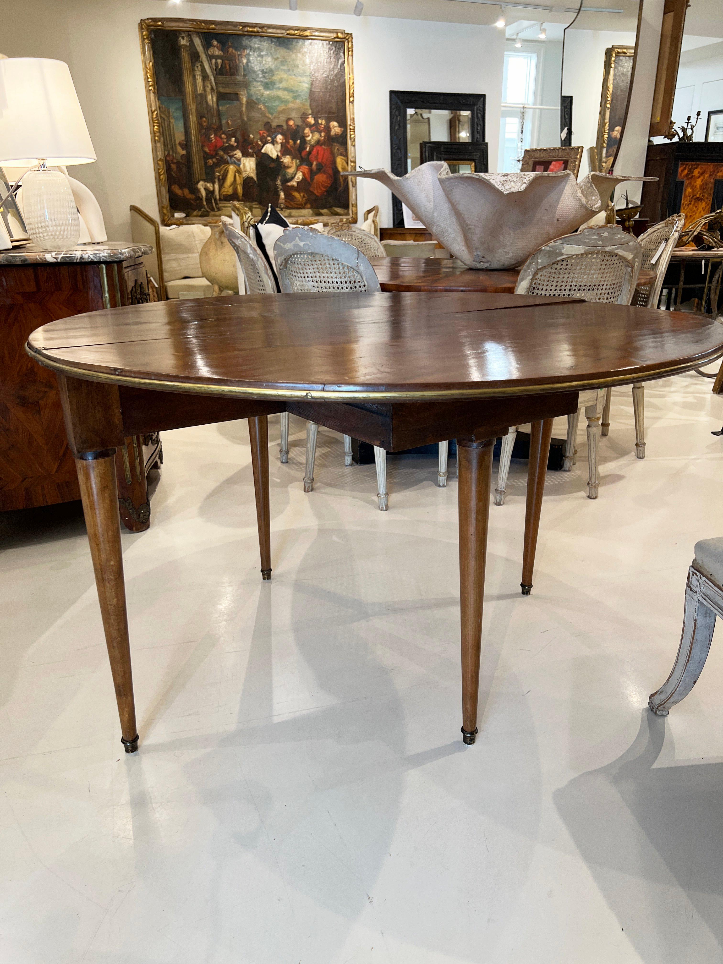 Demi-lune en noyer qui se transforme en table ronde grâce à un pied coulissant.  La circonstance est soulignée par une fine bande de laiton.  Pieds joliment fuselés.