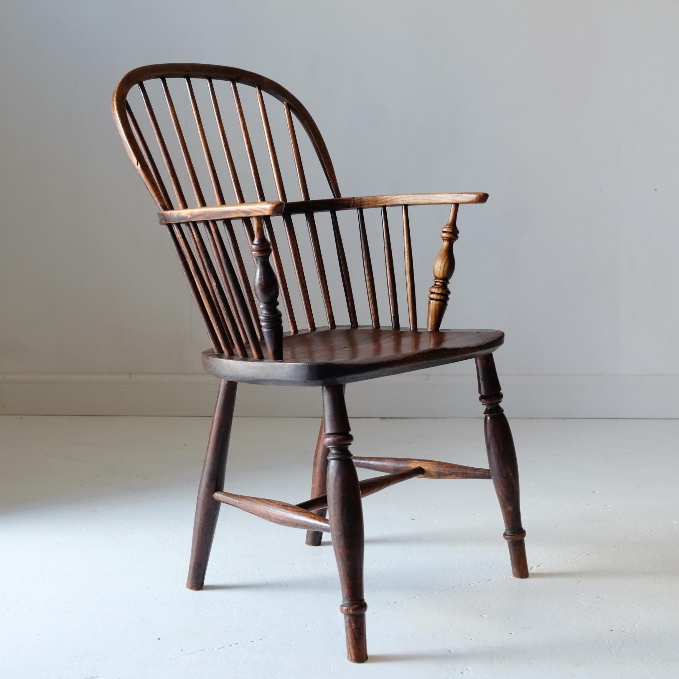 Simple antique low back Windsor chair in ash and elm. Turned legs, united by H stretcher, solid elm seat with nice grain pattern, turned arm supports and stick spindles above and below the single steam bent hoop arms, finishing with a steam bent