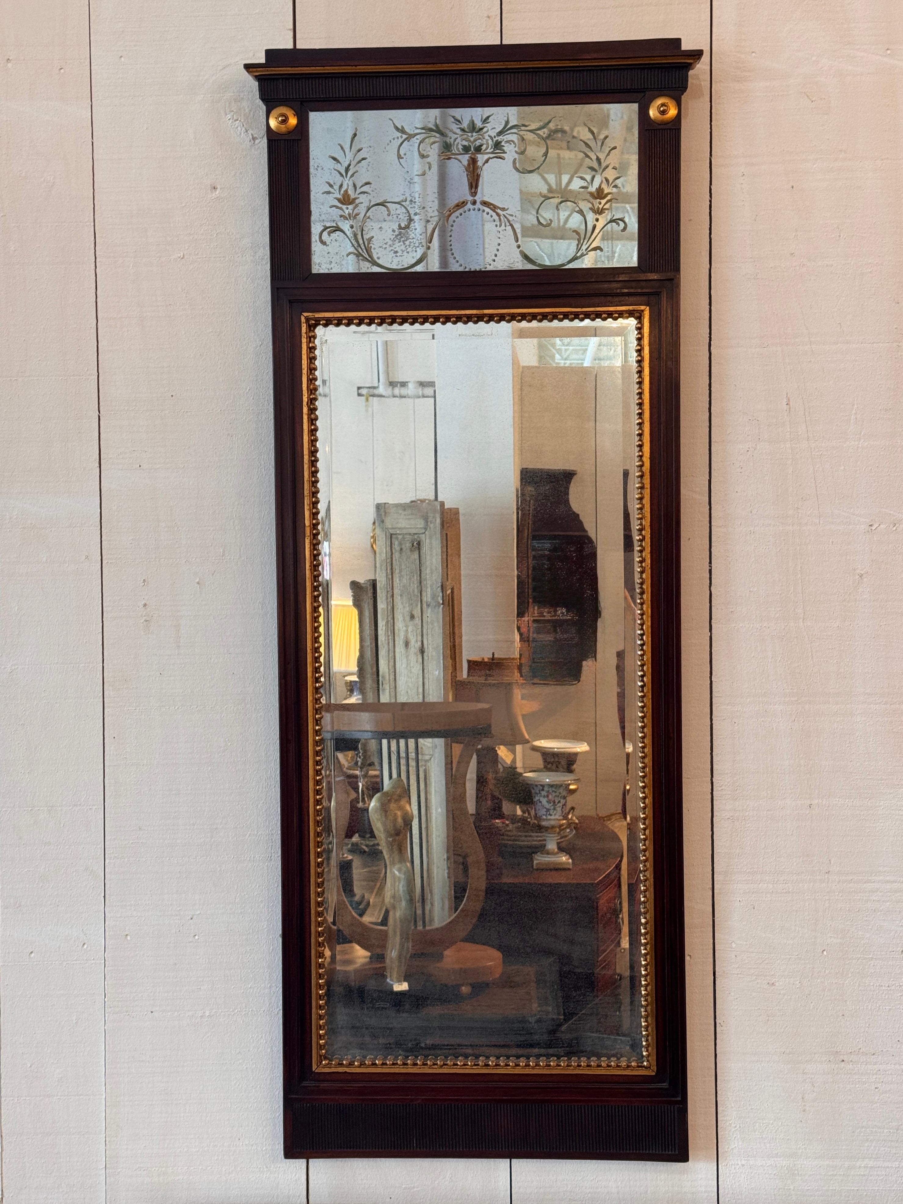 Mahogany mirror with a gilt beaded inner frame and an upper verre églomisé panel painted with scrolling foliage, shown clearly in the detail image. The molded surround features fluted sections and gilt roundels at the crest. The mirror plate