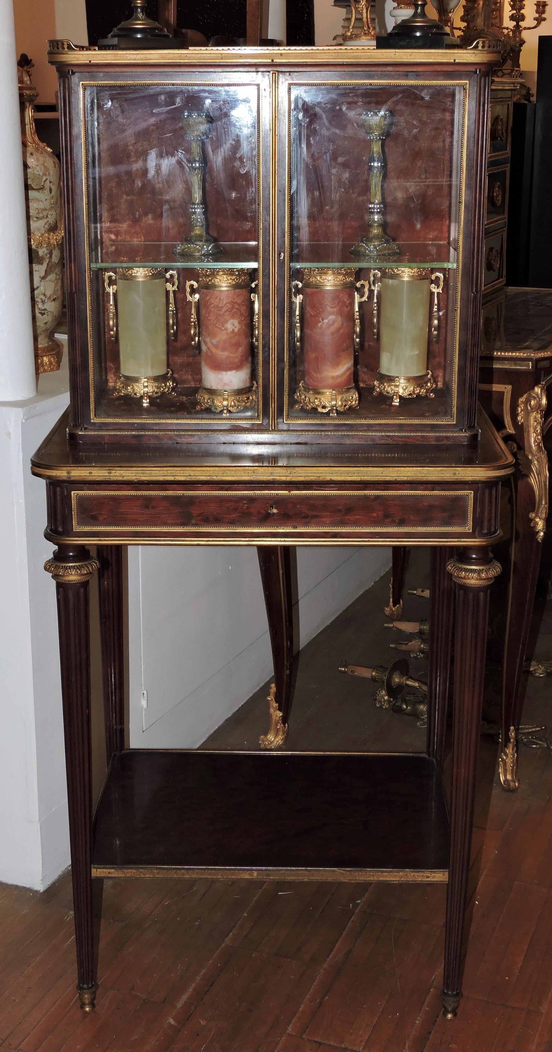 Display window table in speckled mahogany and gilded bronze, opening with a drawer and two glazed leaves, tapered fluted legs and spacer bar.
Louis XVI style,
circa 1880.