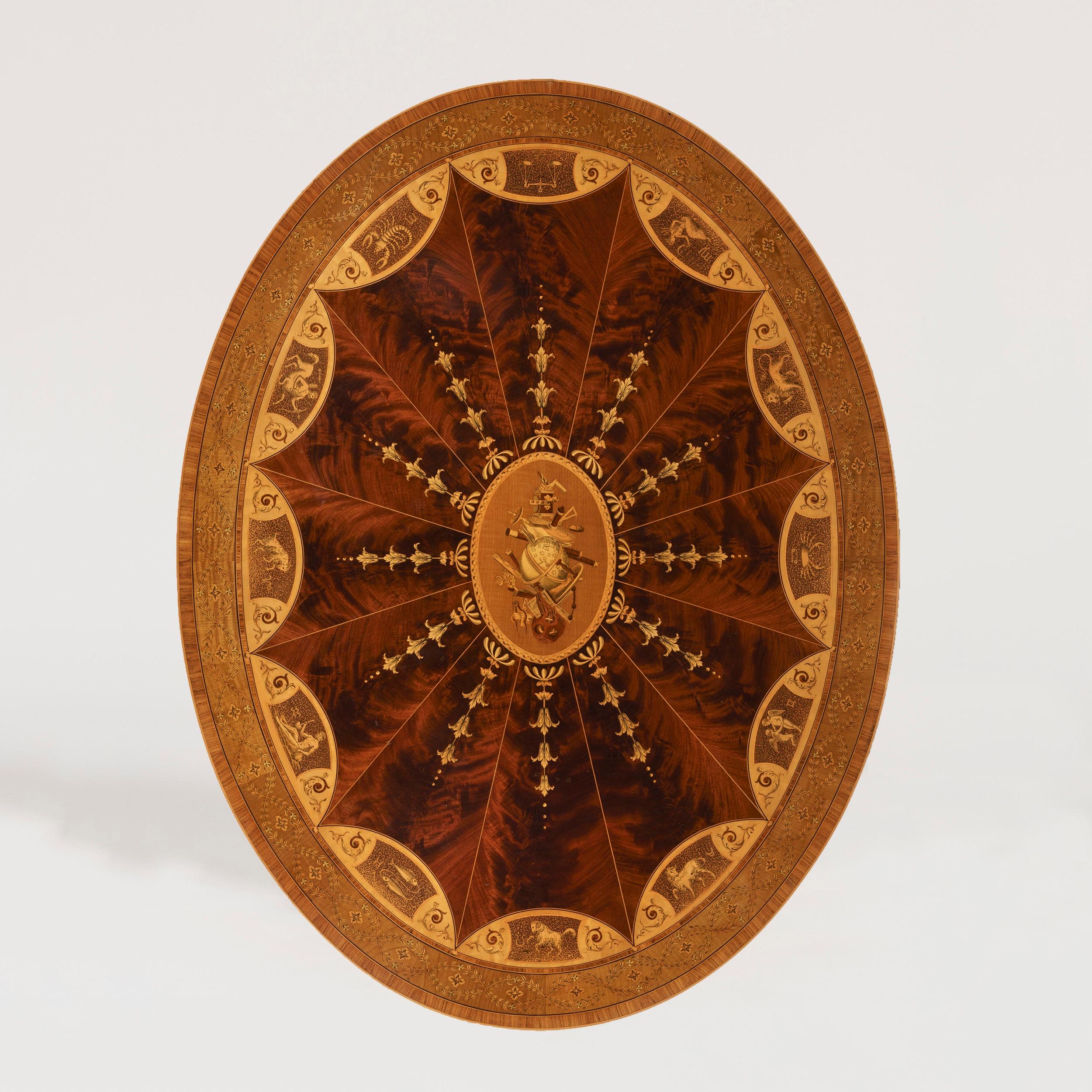 Ein hochwertiger astrologischer Mitteltisch
fest zugeschrieben Maple & Co

Konstruiert in sehr fein gemasertem Mahagoni und Satinholz, und mit Intarsien von höchster Qualität, die von quadratischen Beinen und Spaten Füße auf Rollen, die die ovale