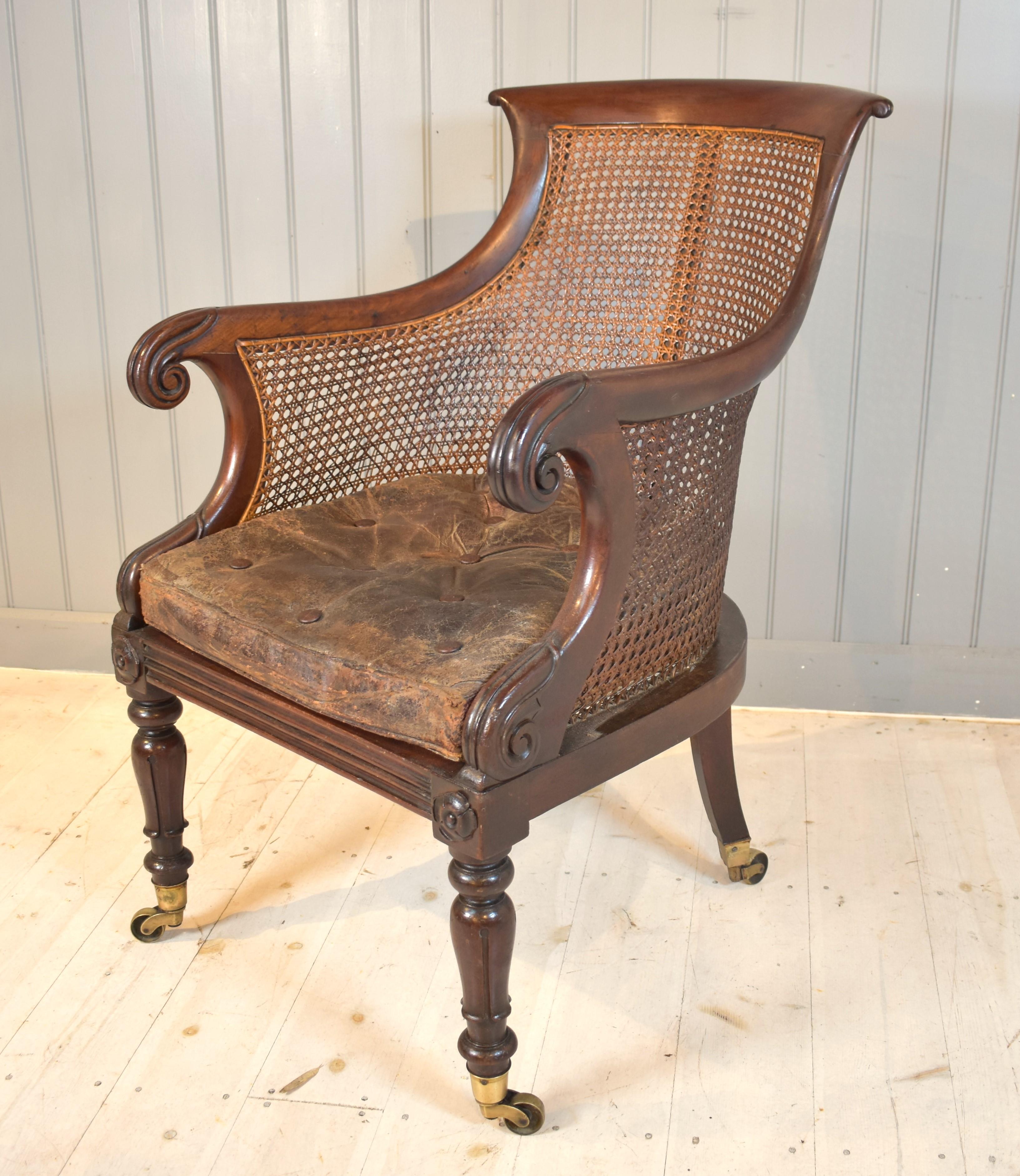 Handsome William IV mahogany library chair, commonly known as a bergere chair. The worn leather cushion is 19th century and the beautifully fluted legs  with carved flower motif show the elegance of design. Above all, the chair is extremely