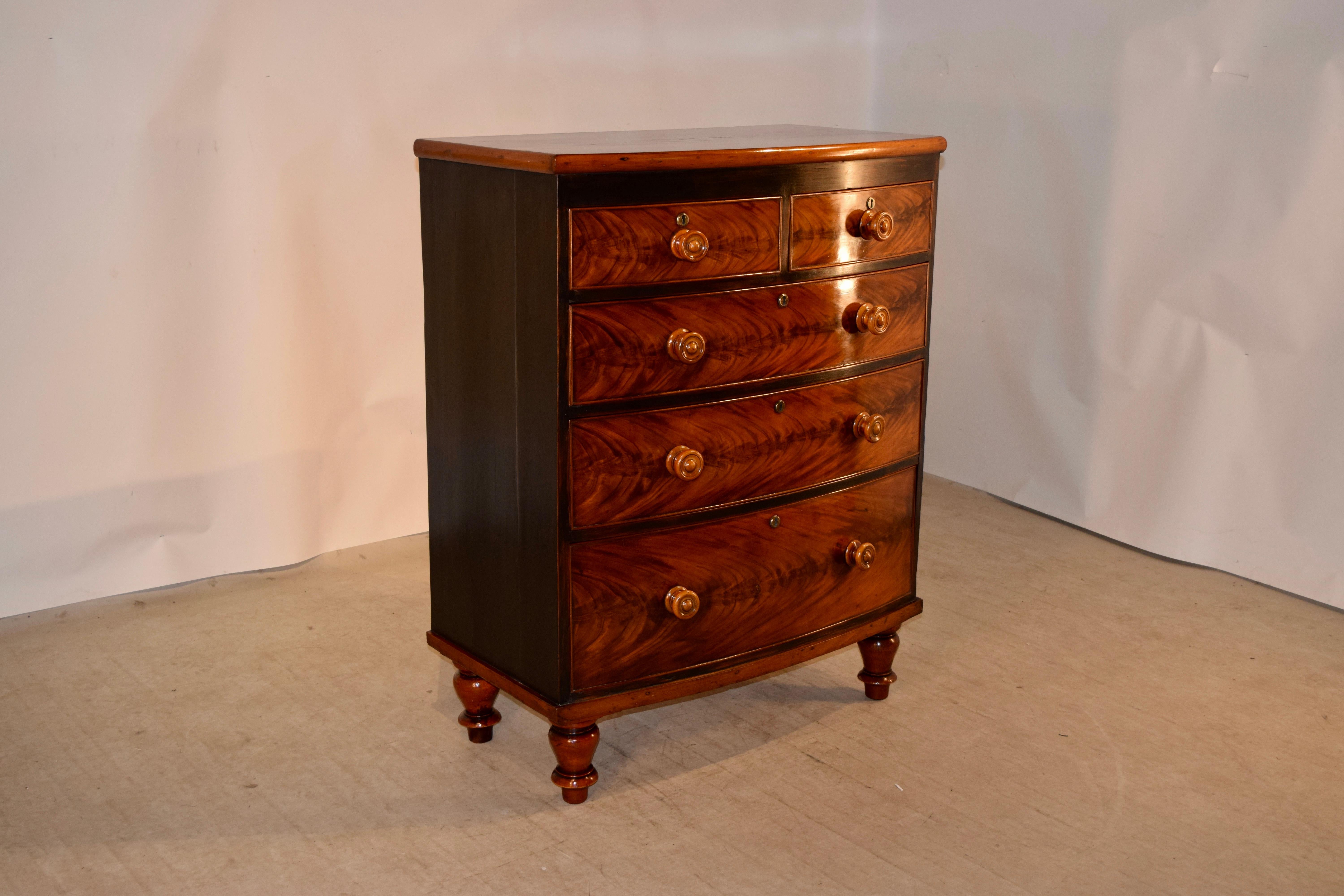 19th century mahogany bow front chest from England. The top has lovely graining and color, and follows down to painted sides and a painted front of the case for contrast with the flame mahogany drawer fronts. The case is raised on hand turned feet.