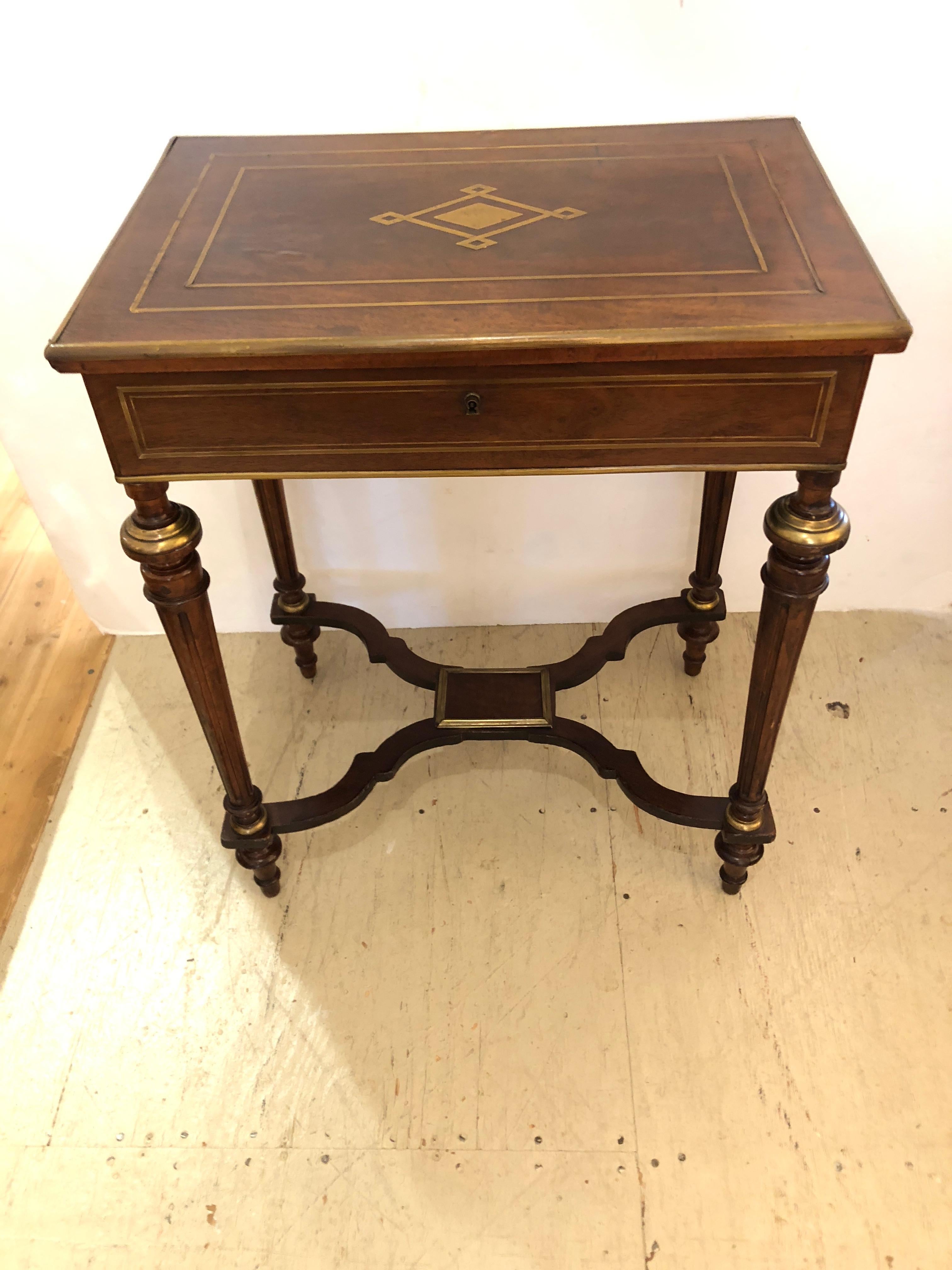 A gorgeous antique inlaid mahogany boule style table having pretty central medallion and brass adornments including on the legs and decorative stretcher at the bottom. The top opens to reveal compartments inside and a mirror.