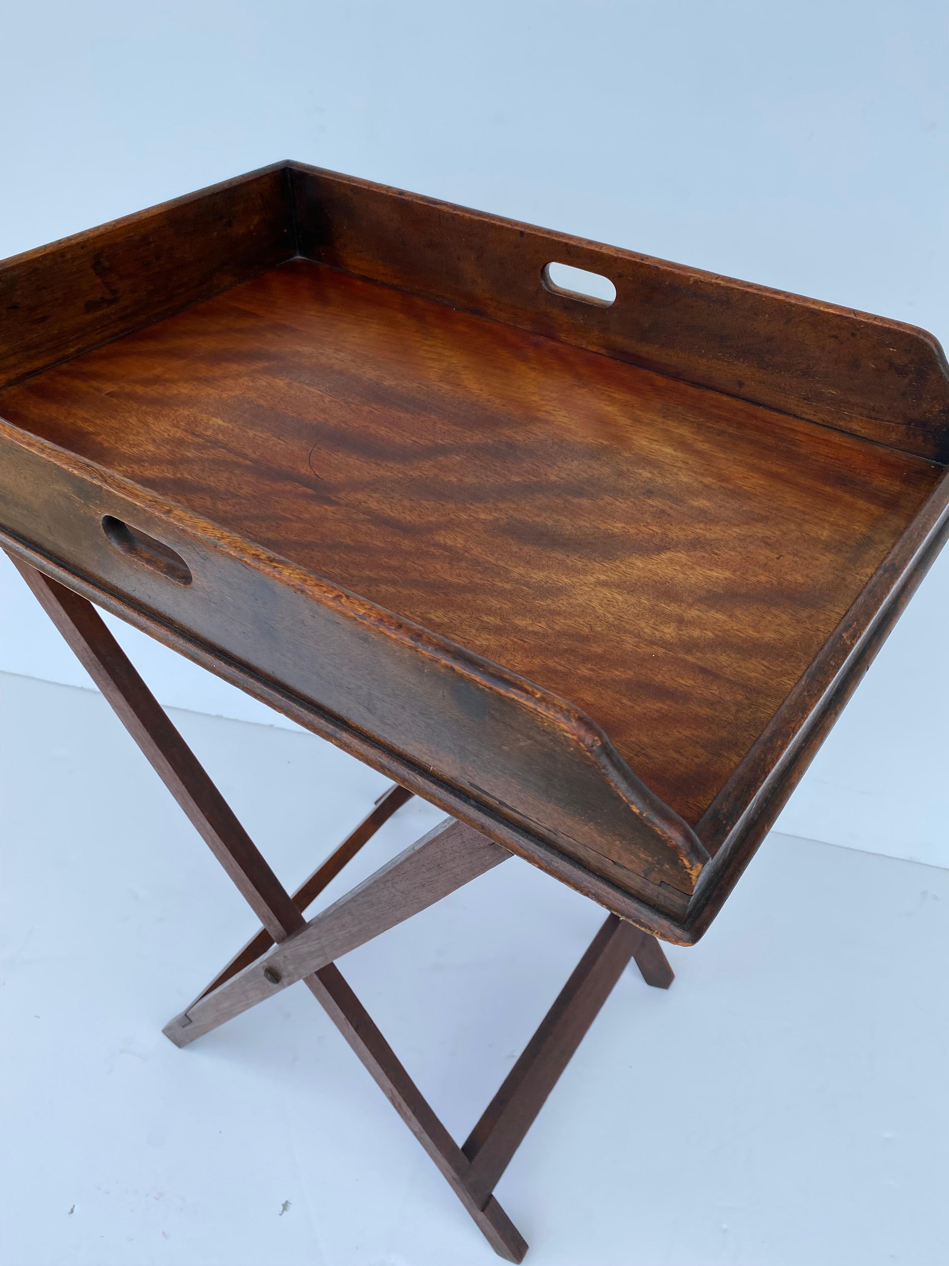 A 19th-century mahogany butler tray on a stand featuring a rectangular-shaped tray with a surrounding gallery.   On a folding X-frame stand with woven straps to accommodate the tray.
