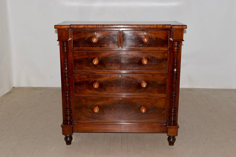 19th century English mahogany chest of drawers with a shaped top and lovely graining, following down to two over three drawers, flanked by hand turned columns and simple sides. The base in banded and is supported on hand turned feet.