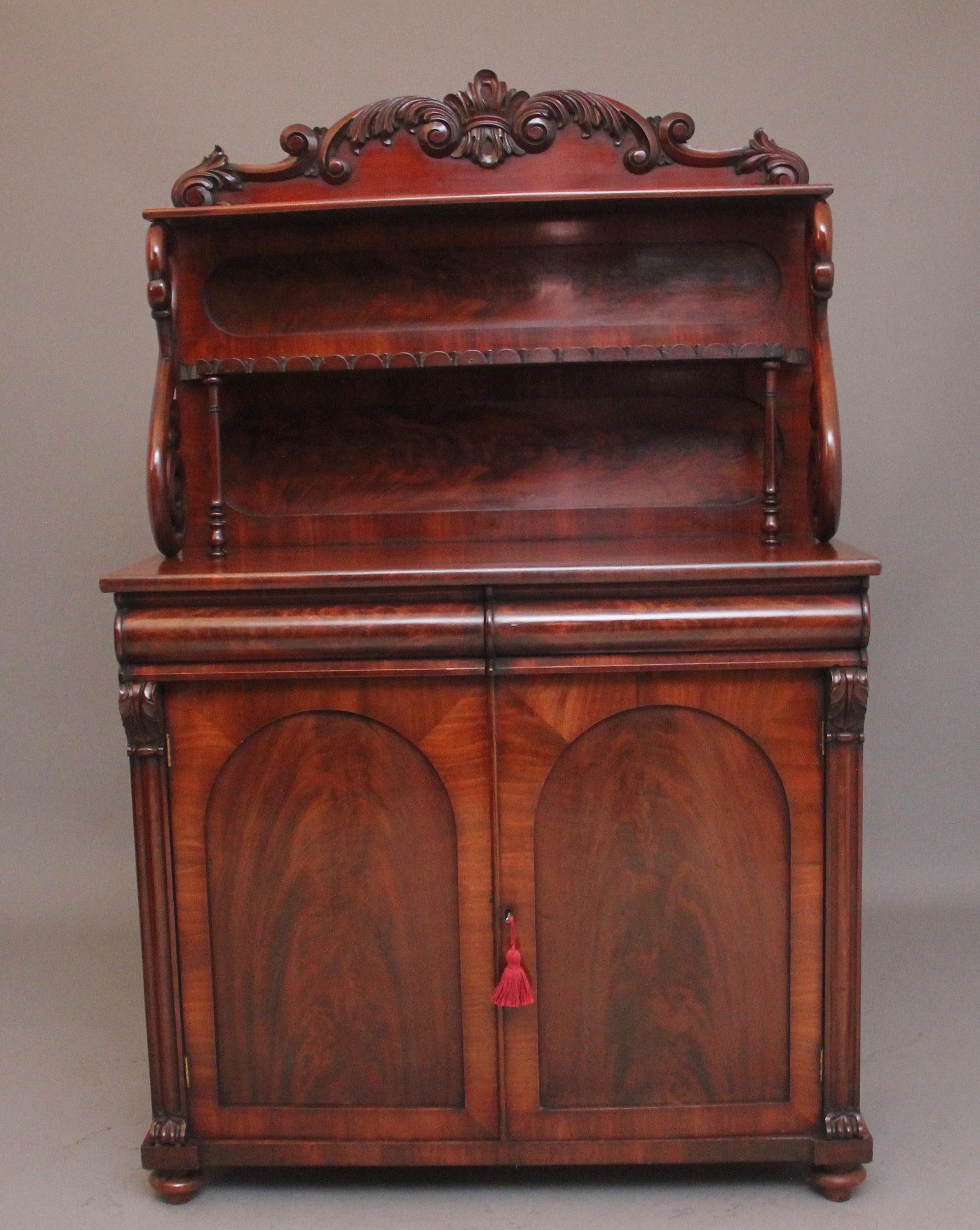 A lovely quality mid 19th Century flame mahogany chiffonier / cabinet,  having a shaped and moulded carved scrolled pediment above a two shelves with oval flame mahogany back panels, the bottom shelf supported on turned finials and the shelf having