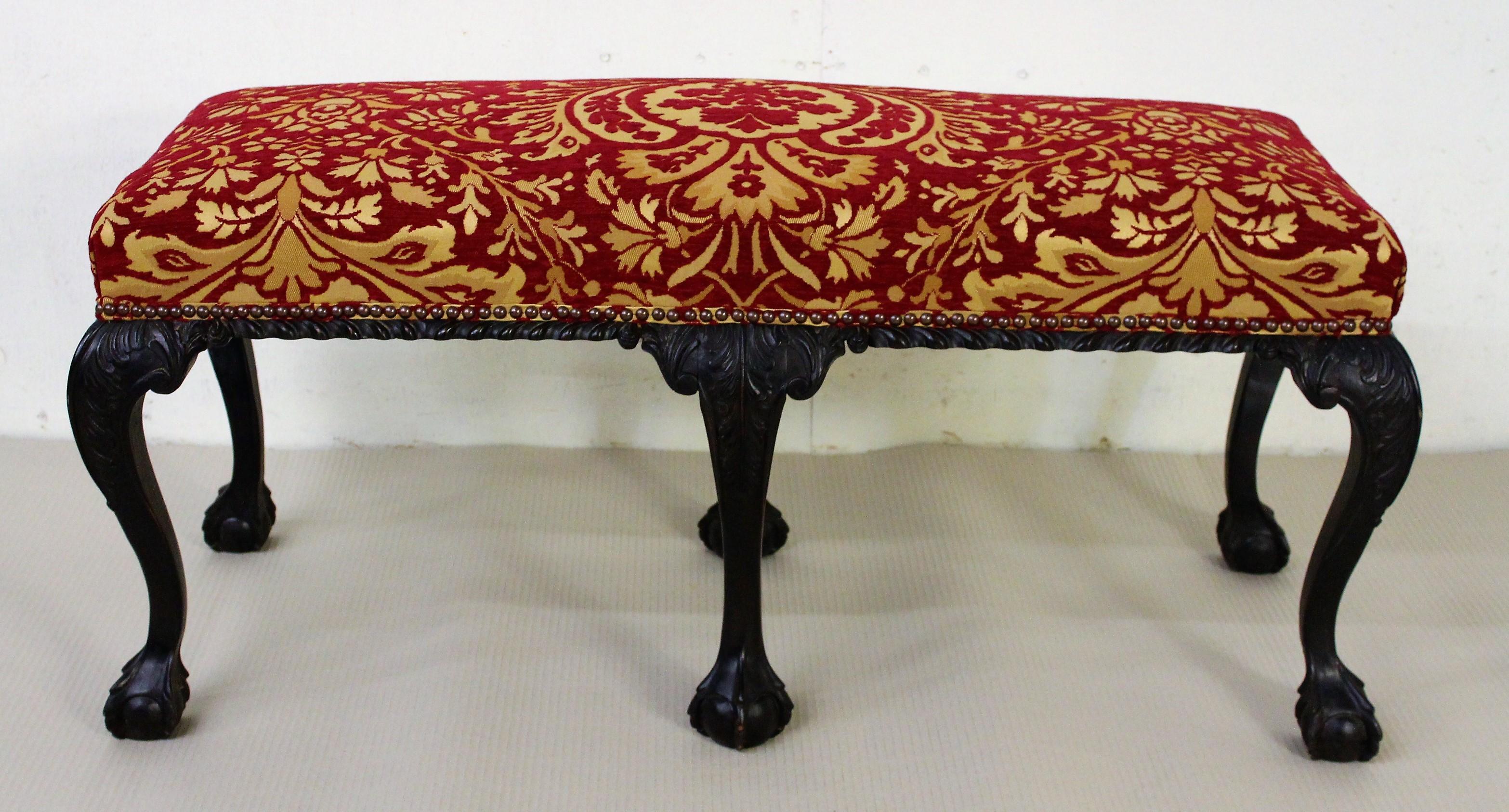 A bold and impressive late 19th century mahogany upholstered stool in the manner of Thomas Chippendale. Well-constructed in solid mahogany with crisply carved decorations. With 6 legs, each terminating in characteristic ball and claw feet. Would sit