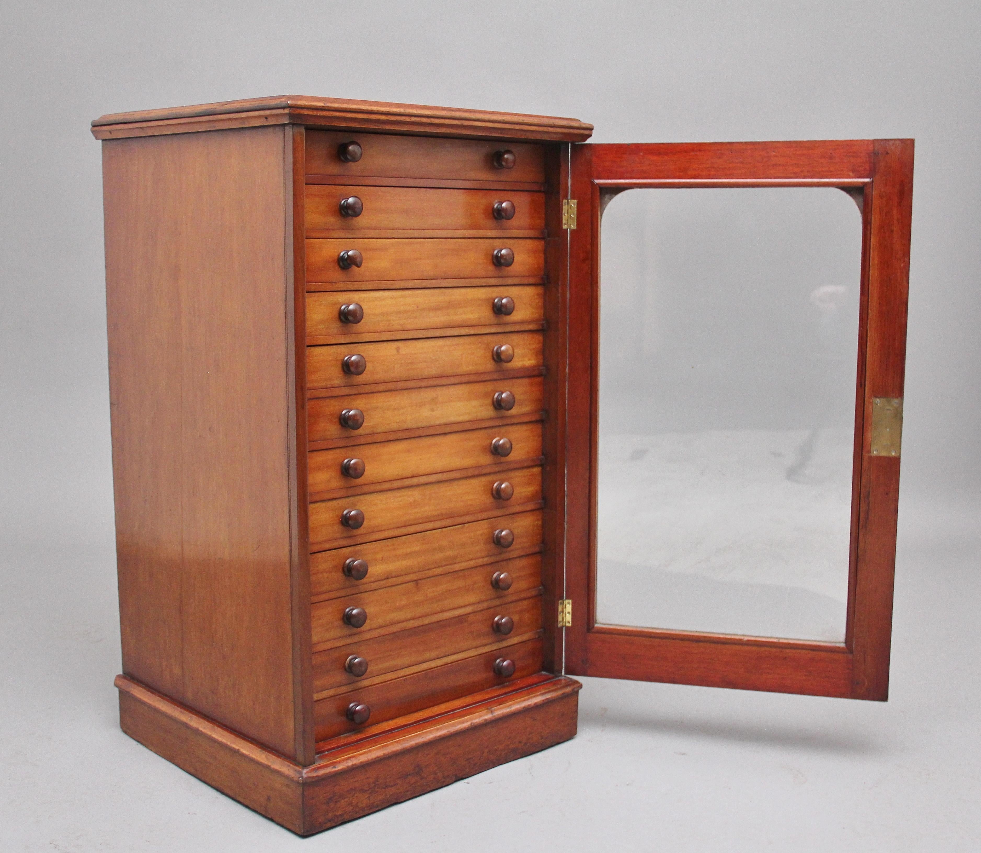 19th Century mahogany collectors / specimen cabinet, the thumb moulded edge top above a single glazed door with arched moulding surround opening to reveal twelve glass topped drawers, all with the original turned wooden knob handles, all the drawers