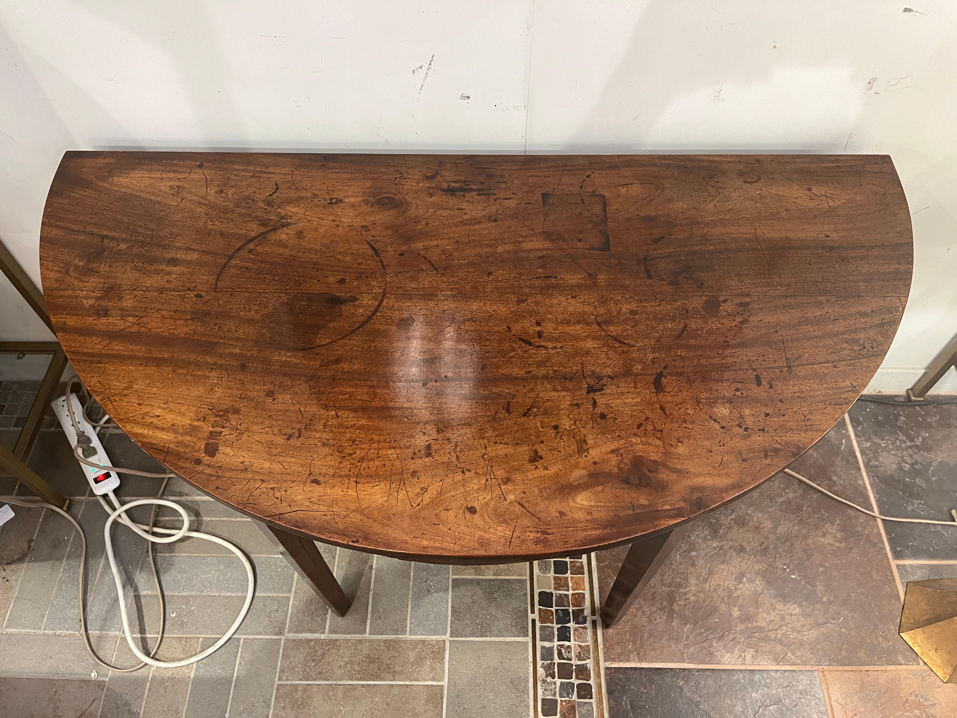 Crafted in the elegance of the 19th century, this mahogany demi-lune console table possesses timeless charm. Its rich, aged mahogany surface displays the years of loving use, accentuating the intricate grain patterns and luxurious hue. The