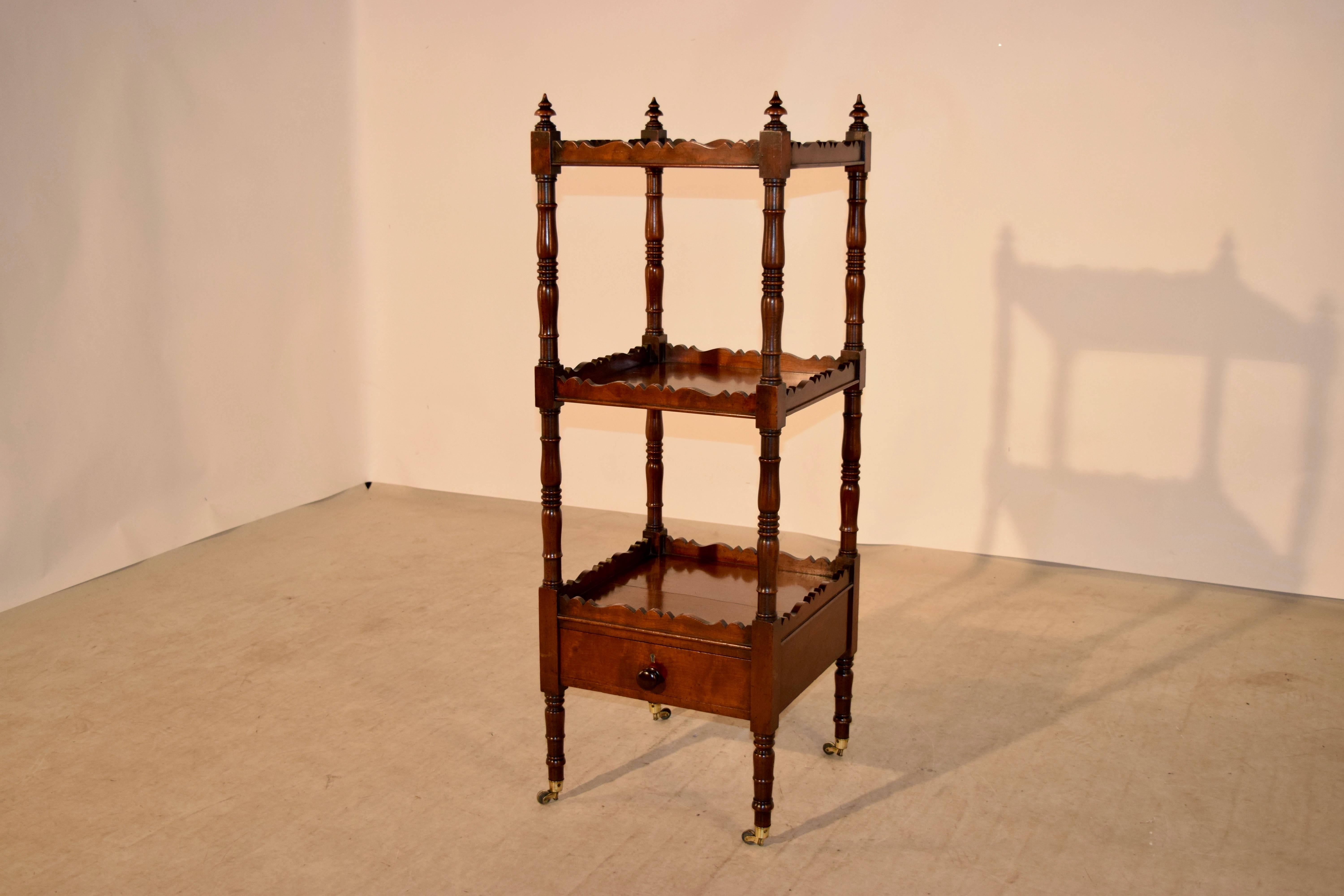 19th century English etagere made from Mahogany. It has three shelves, separated with hand turned shelf supports and has scalloped galleries and finials on top. There is a single drawer at the base and it is raised on hand-turned legs.