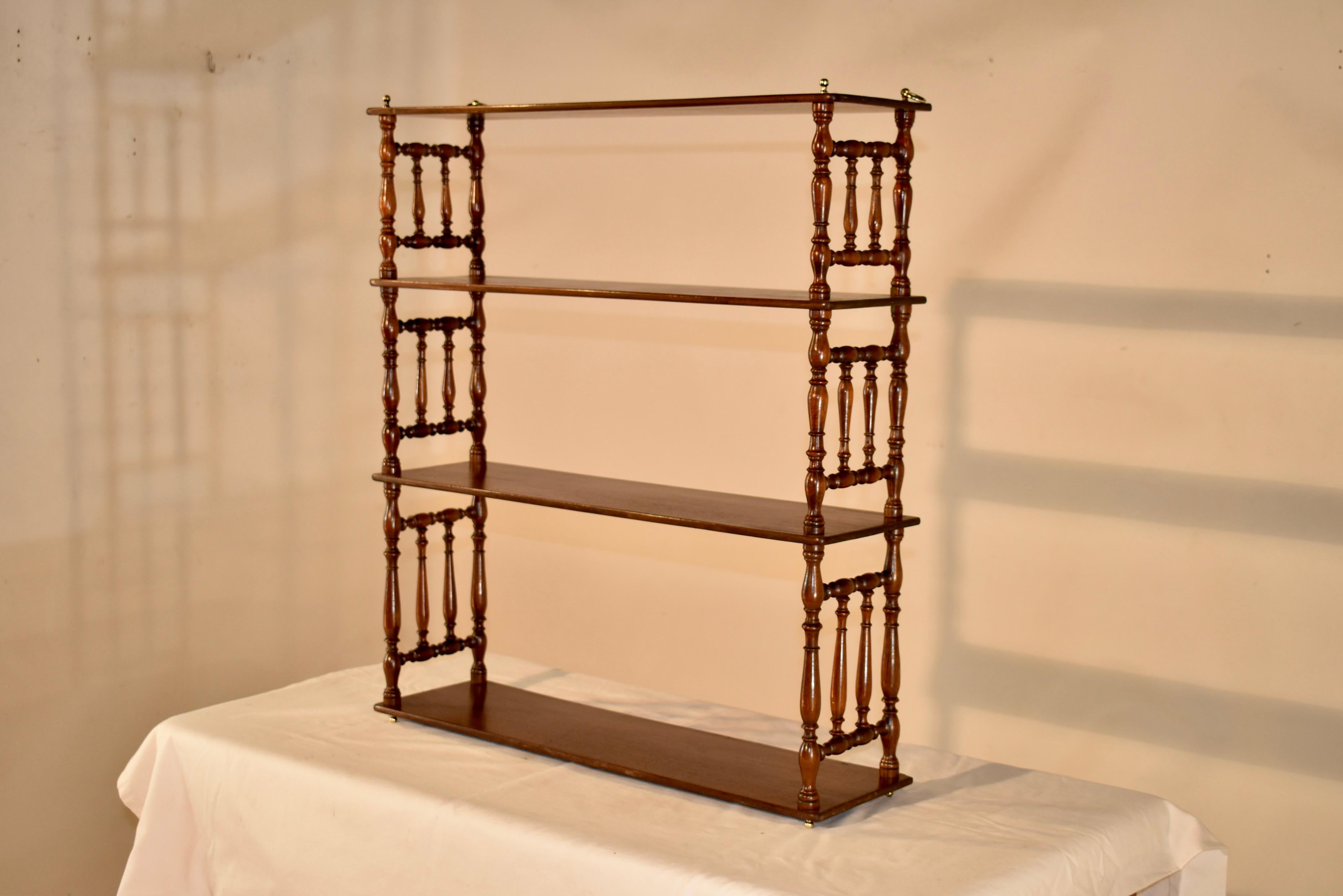 19th century mahogany shelf from England. The top and base have brass finials, following down to three shelves, all made from single boards. The shelves are separated by wonderfully hand turned shelf supports, which give the shelf a lovely profile.