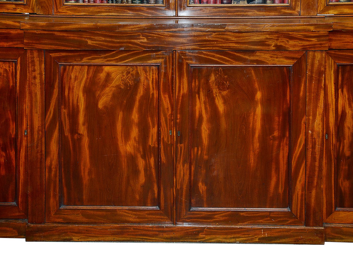 A very good quality early 19th century flamed mahogany break fronted Library bookcase, Having four glazed doors above, enclosing adjustable shelves with tooled leather trim, four inset panelled doors beneath and raised on a plinth base.