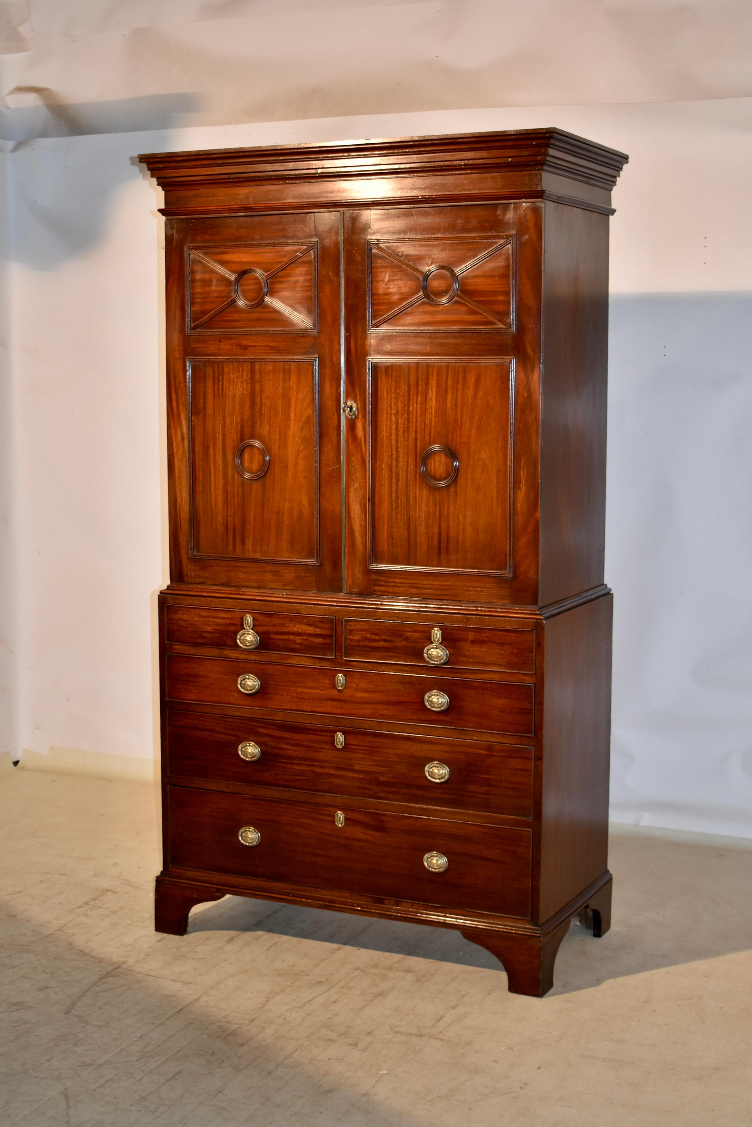 19th century linen press from England and made from mahogany.  The top has a lovely crown molding over simple sides, made from single boards.  The front has two hand paneled doors, which open to reveal three linen slide drawers, over the base which