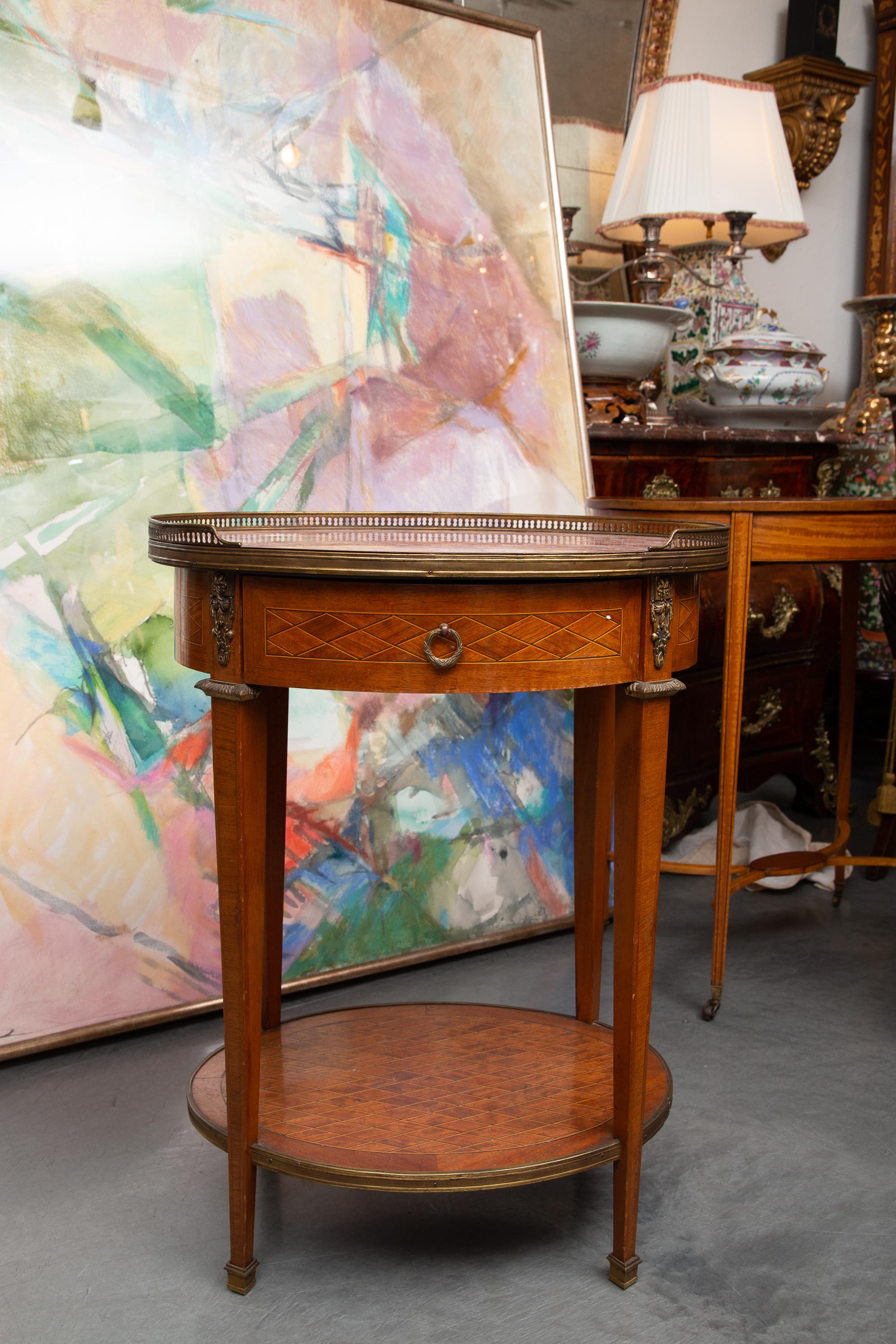 This is a lovely late 19th century mahogany side table with an oval rouge marble top framed by a pierced brass gallery over a conforming parquetry frieze with central drawer, raised on square tapered legs joined by a platform stretcher.